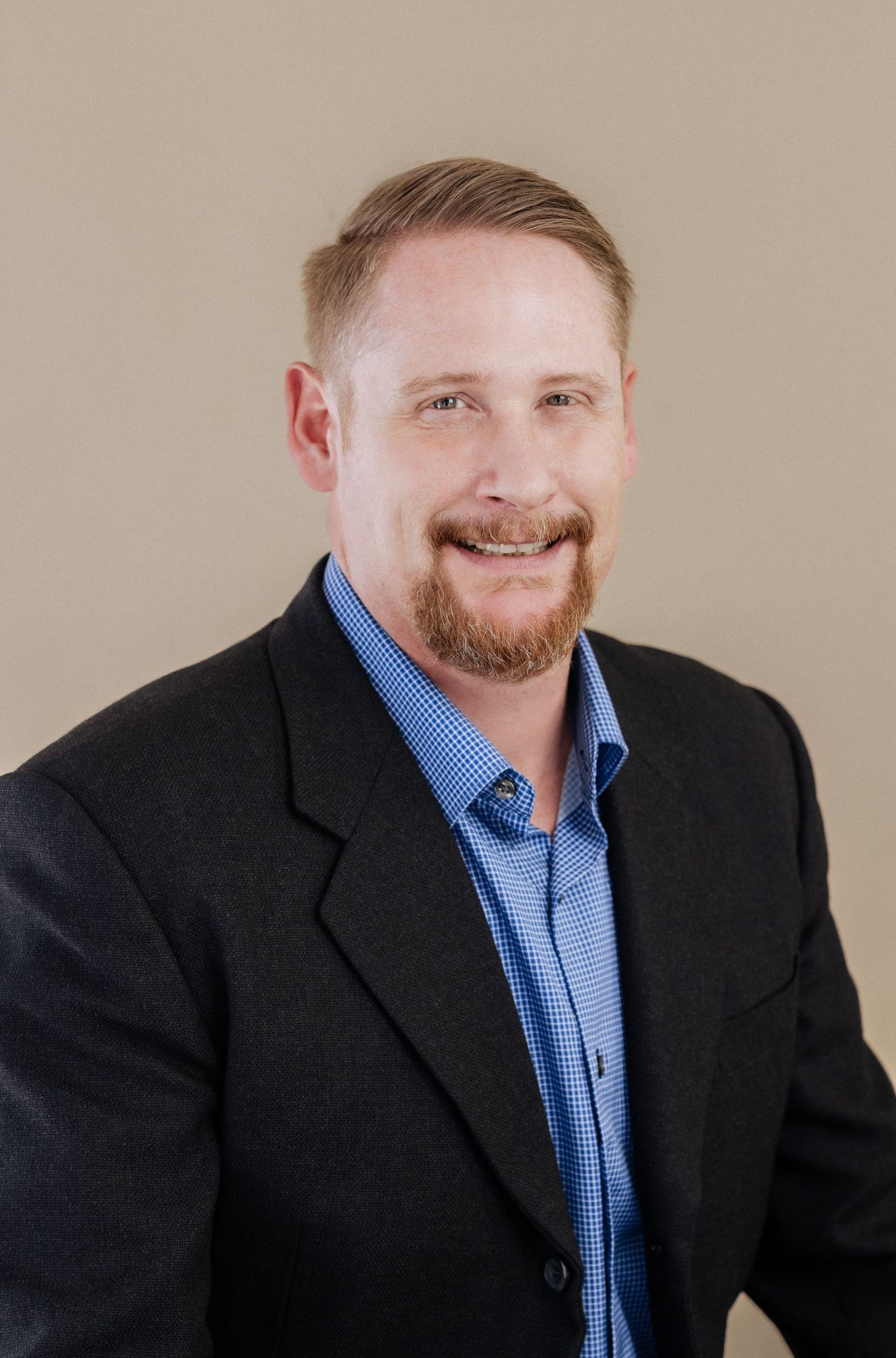 Professional headshot of a person wearing a blue button-up shirt and dark blazer against a neutral background.