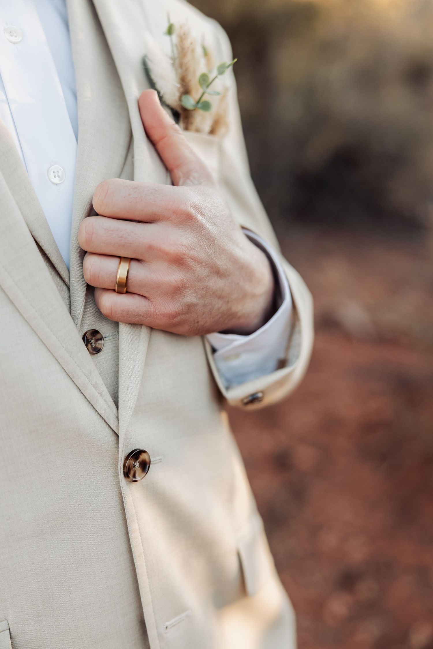 Close-up of a cream suit jacket with boutonniere and wedding ring detail.