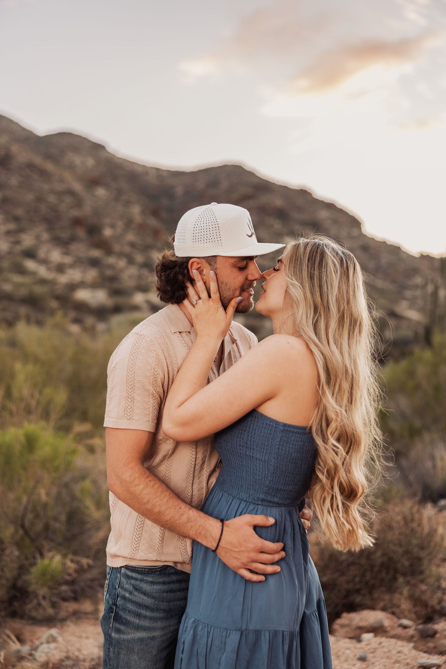 A couple embraces intimately against a backdrop of desert mountains during golden hour.