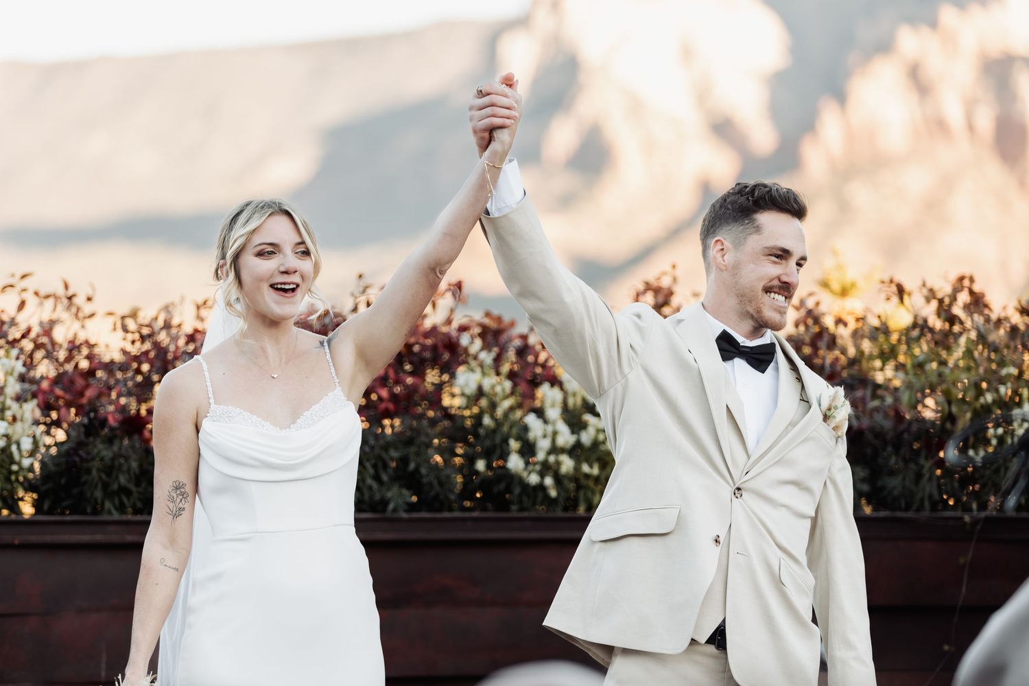 Wedding couple dances and laughs together on a sunset rooftop terrace surrounded by floral landscaping.