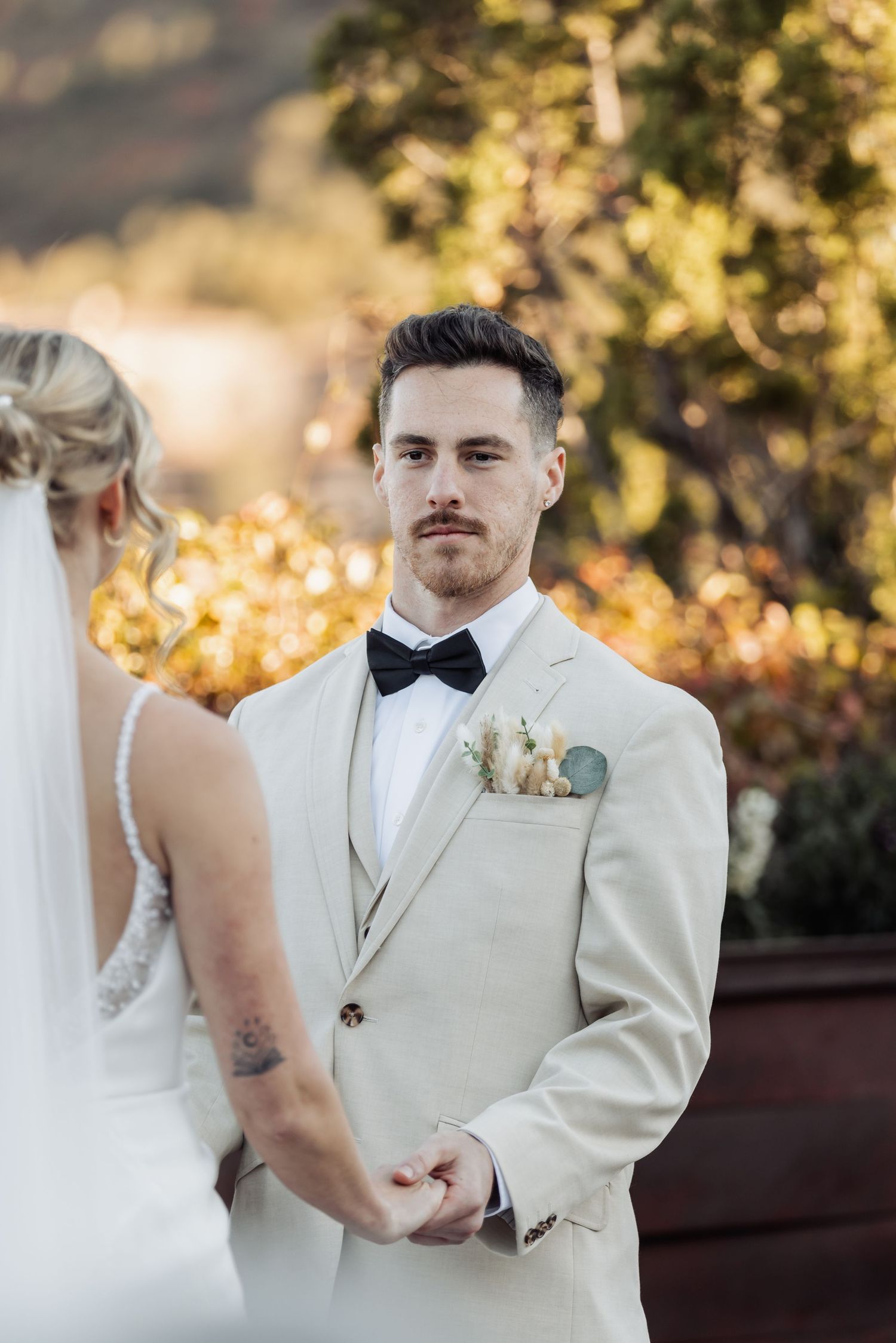 A wedding moment captured at sunset showing formal attire in cream and black with golden sunlight in background.