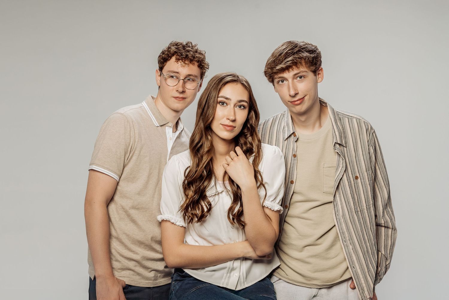 Three people pose together against neutral backgrounds wearing beige and white casual clothing in a modern studio photoshoot.