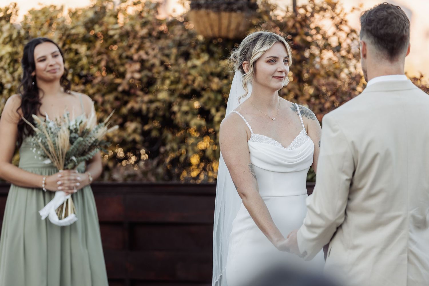An outdoor wedding ceremony with the wedding party in sage green and neutral attire against an autumn backdrop.