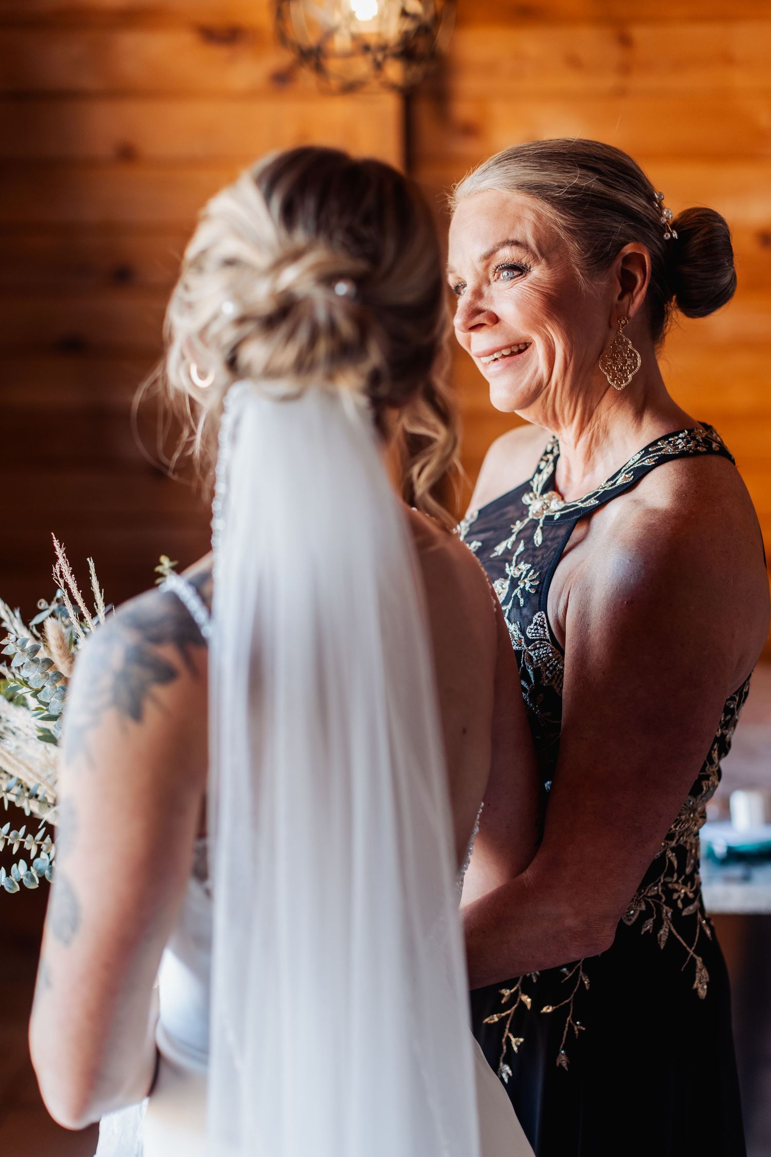 A joyful wedding preparation moment captured in warm wooden cabin lighting with an elegant bridal veil.