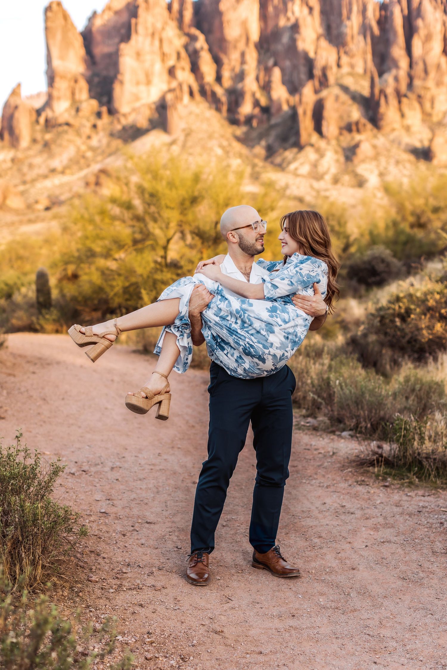 Playful couple moment captured on desert trail with towering cliffs in the background.