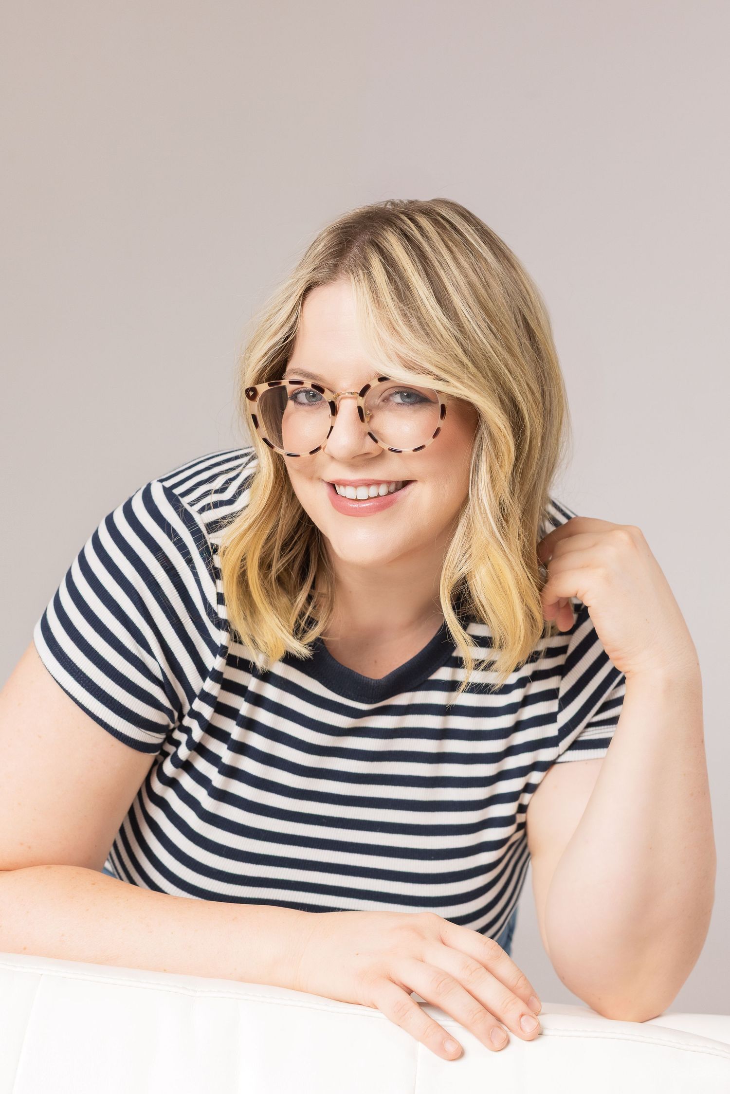 Side view of person in striped t-shirt resting on white surface with genuine smile and blonde hair.