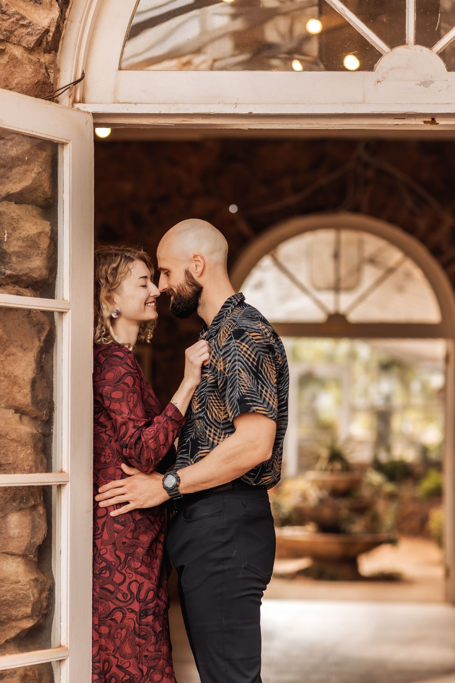A couple in coordinated outfits share an intimate moment by a stone archway with decorative lighting.
