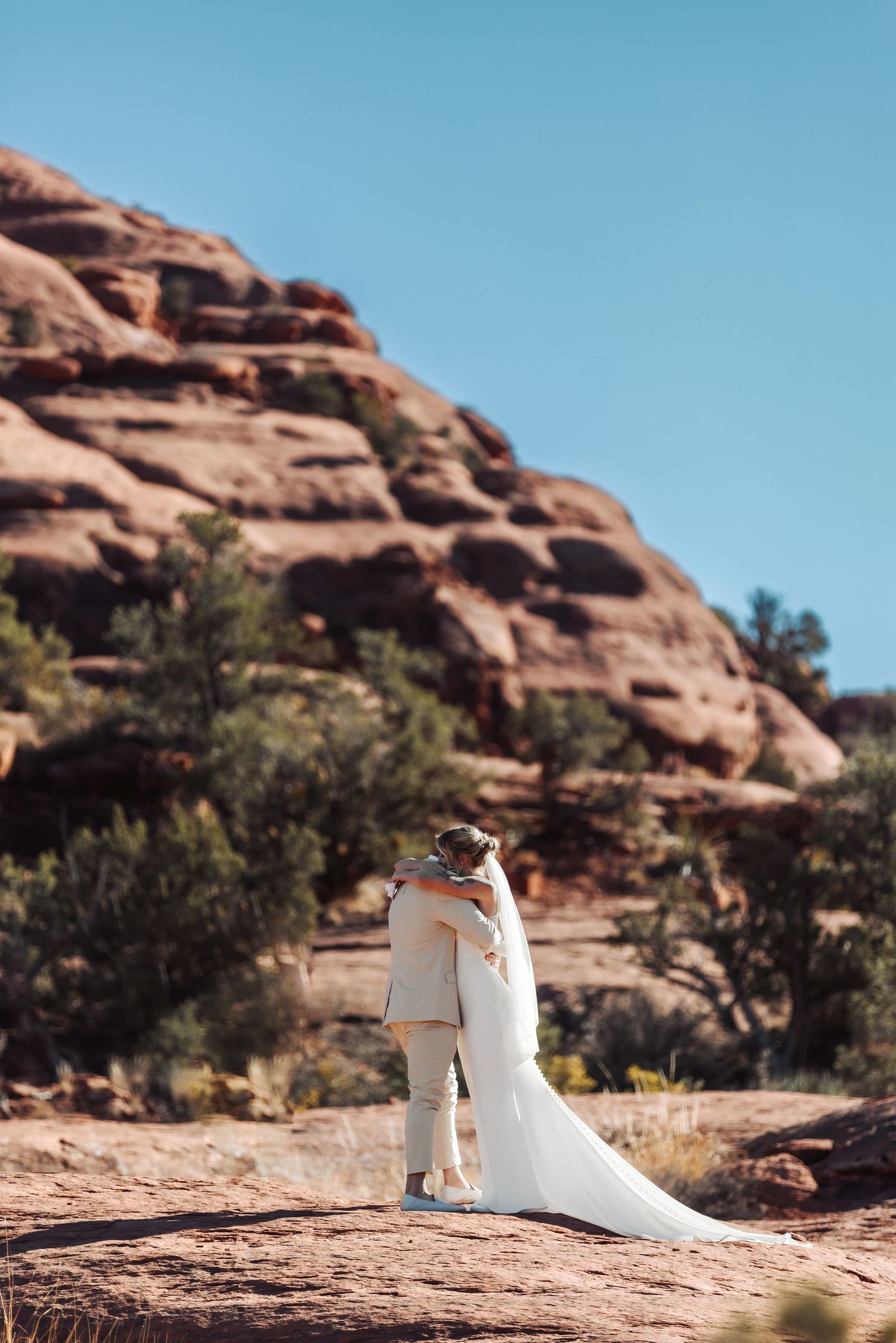 A couple shares an intimate moment during their wedding photoshoot among red rock formations in the desert landscape.