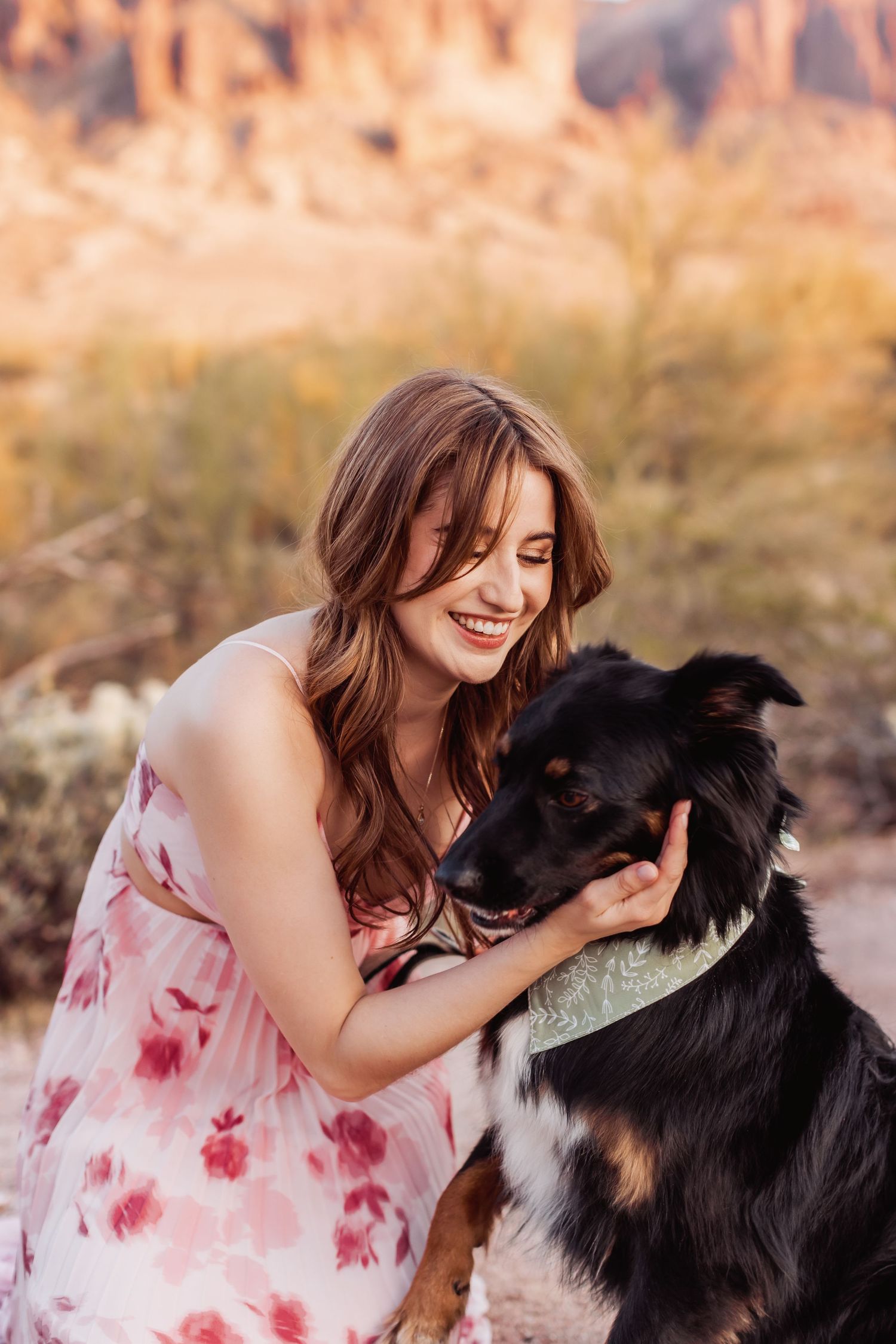 Woman in pink floral dress shares a joyful moment with her black and white Border Collie in a desert landscape.