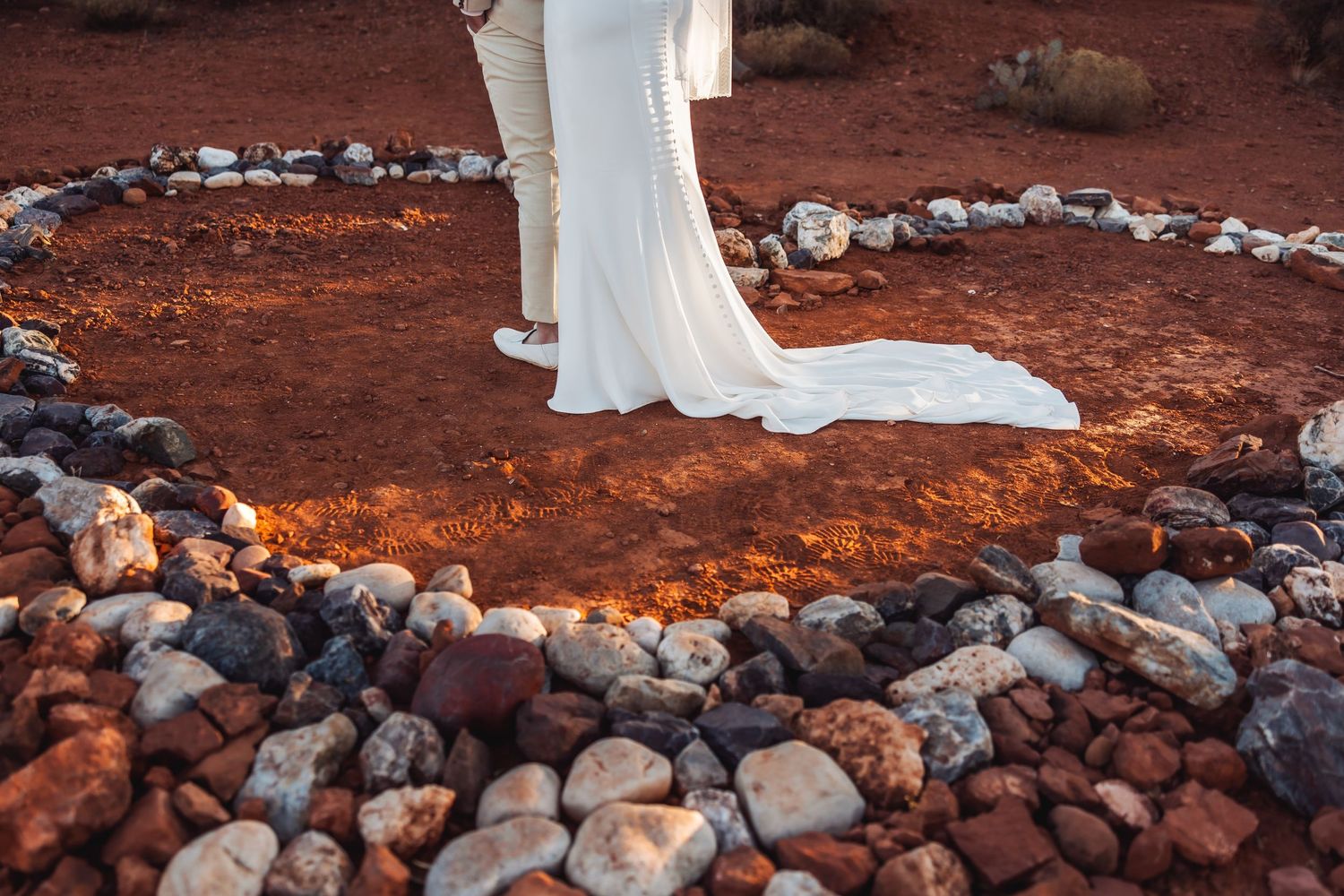 Long white wedding dress train flows over red desert soil surrounded by a heart-shaped stone border.
