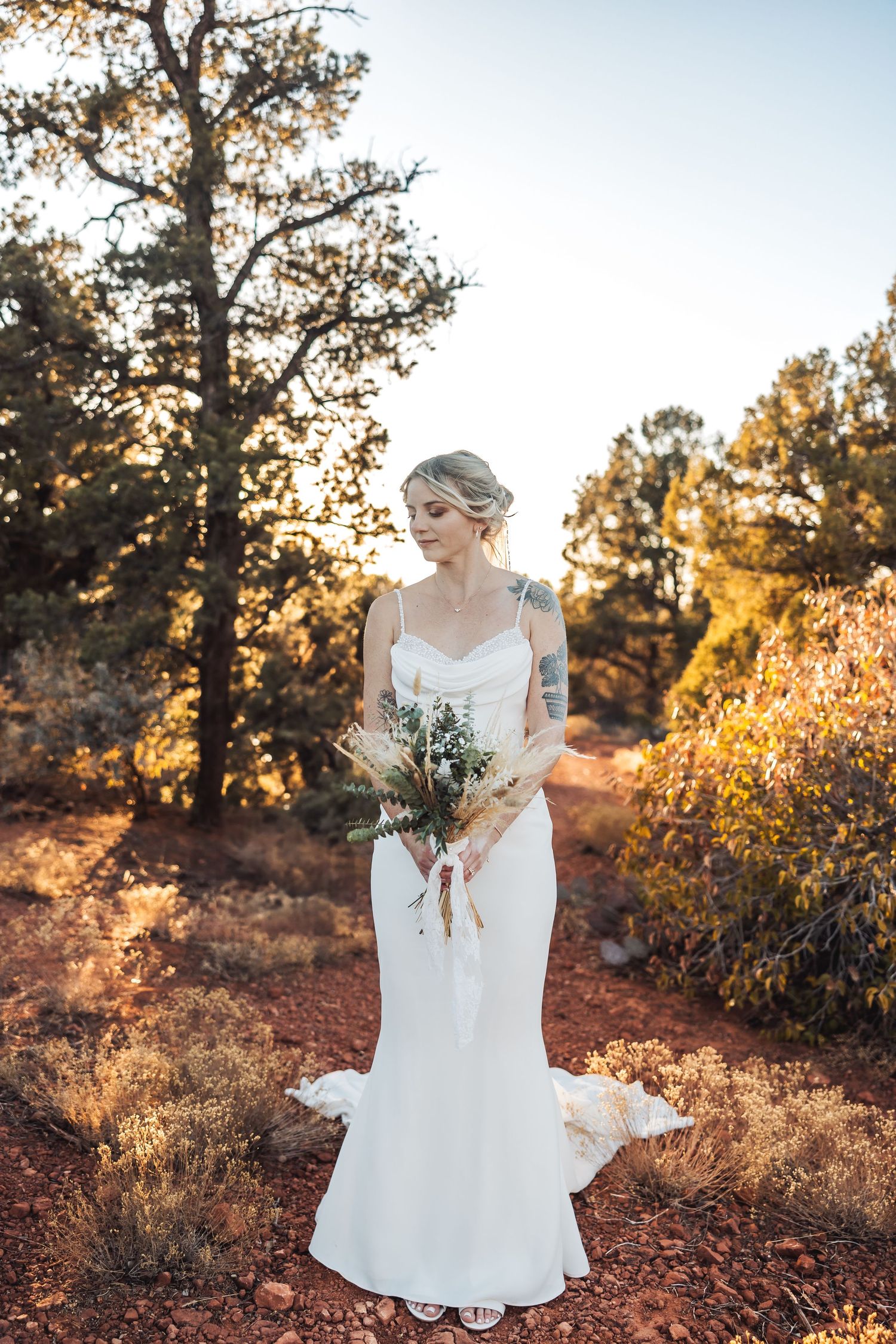 Elegant white wedding dress contrasts with rustic red desert landscape at golden hour.