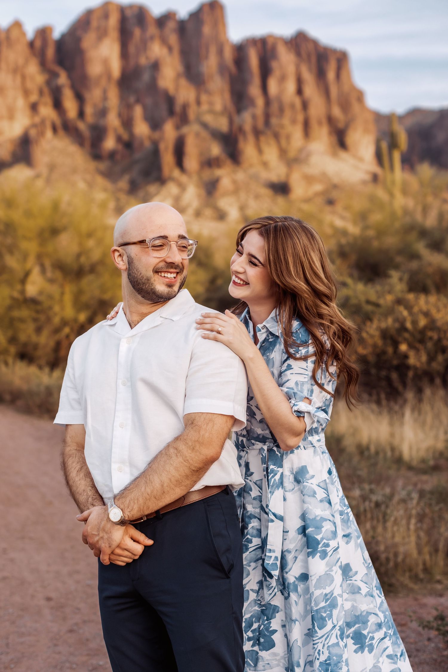 A couple shares a romantic moment on a dirt path with the majestic Superstition Mountains rising in the background.
