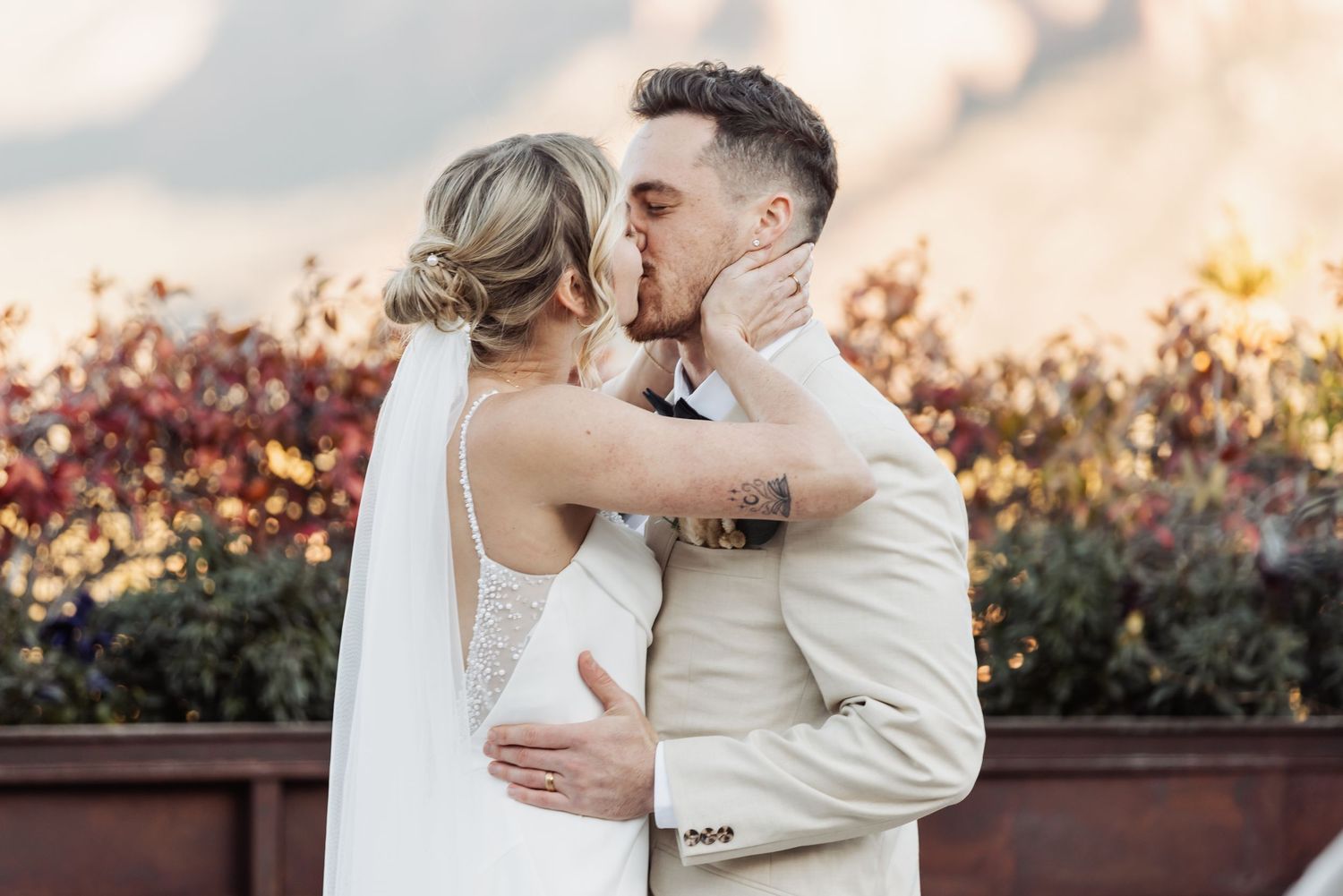 A romantic wedding moment captured during sunset with colorful autumn foliage in the background.