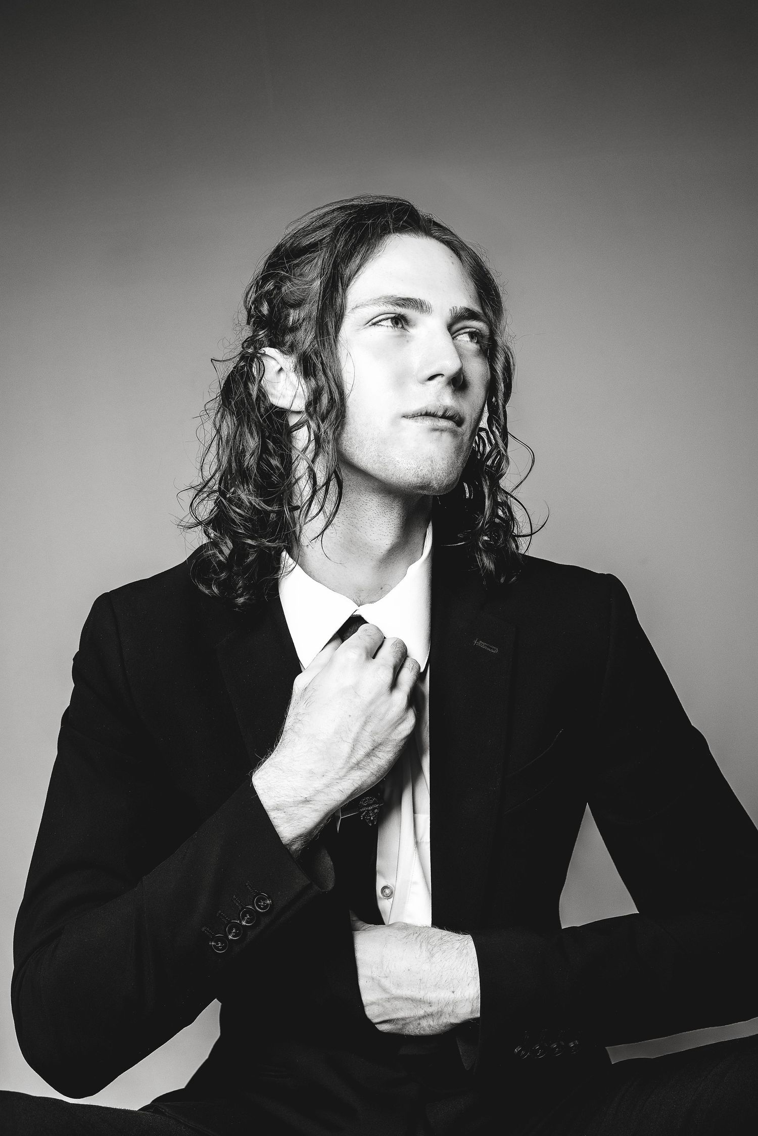A dramatic black and white portrait series showing a person in a dark suit striking contemplative poses.