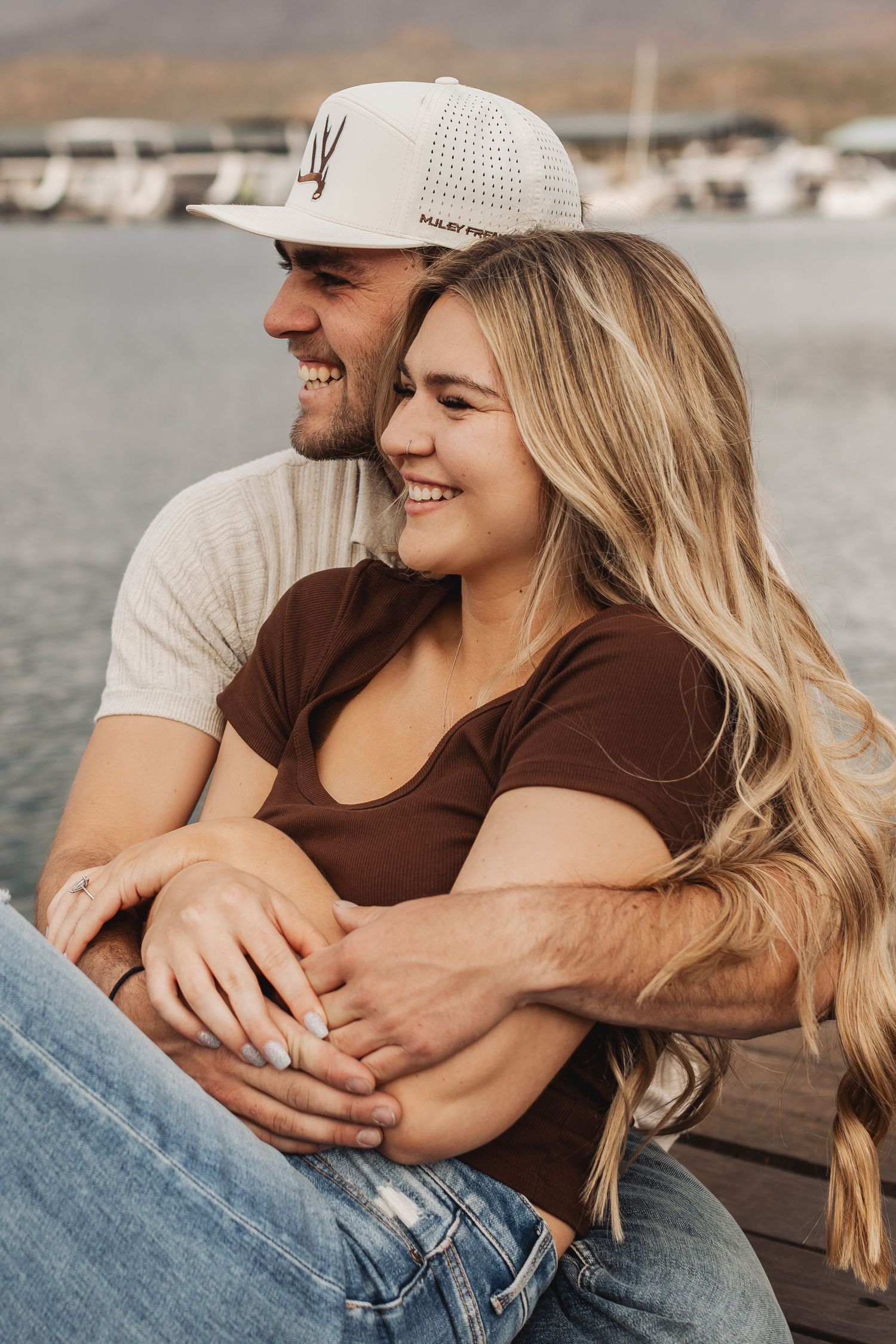 Happy couple embraces by marina as they snuggle and laugh together on sunny afternoon.