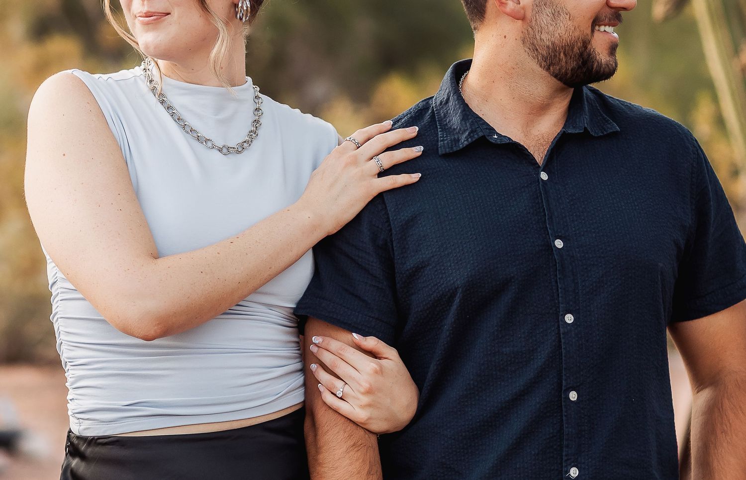 Couple wearing matching gray and navy outfits poses together in sunlit outdoor setting during photo session.
