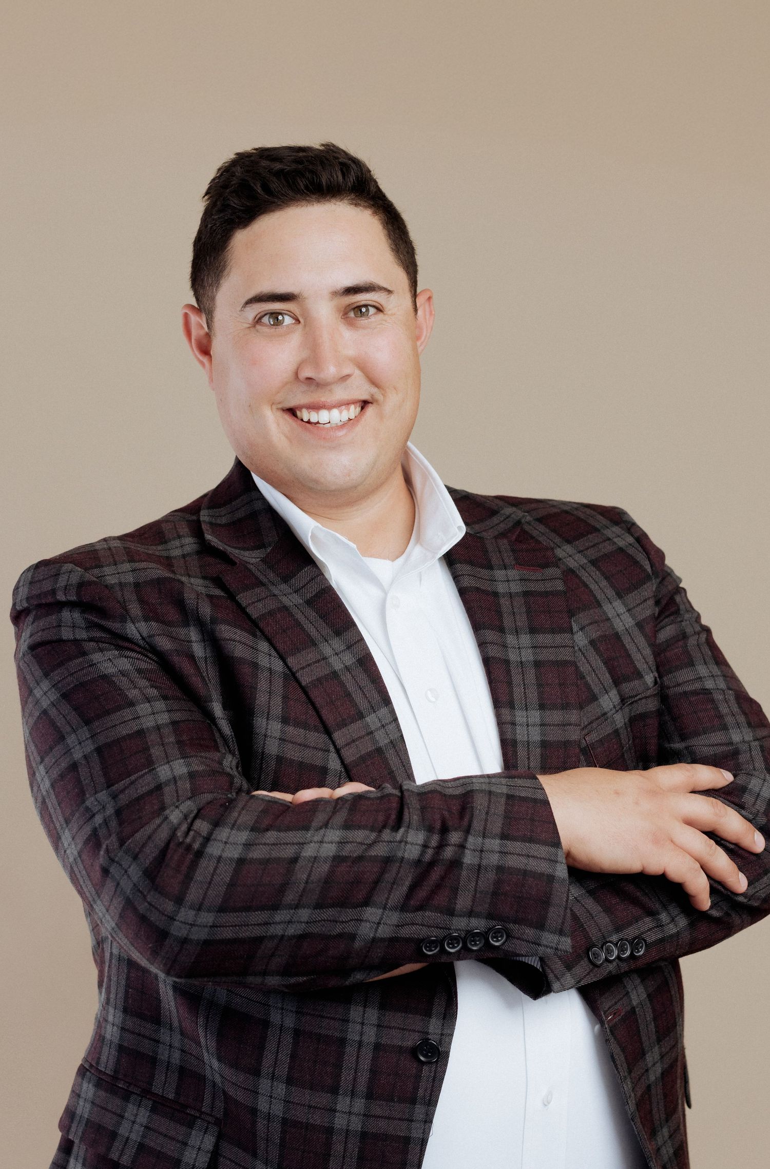Professional portrait of someone in a plaid blazer and white dress shirt posing with arms crossed.