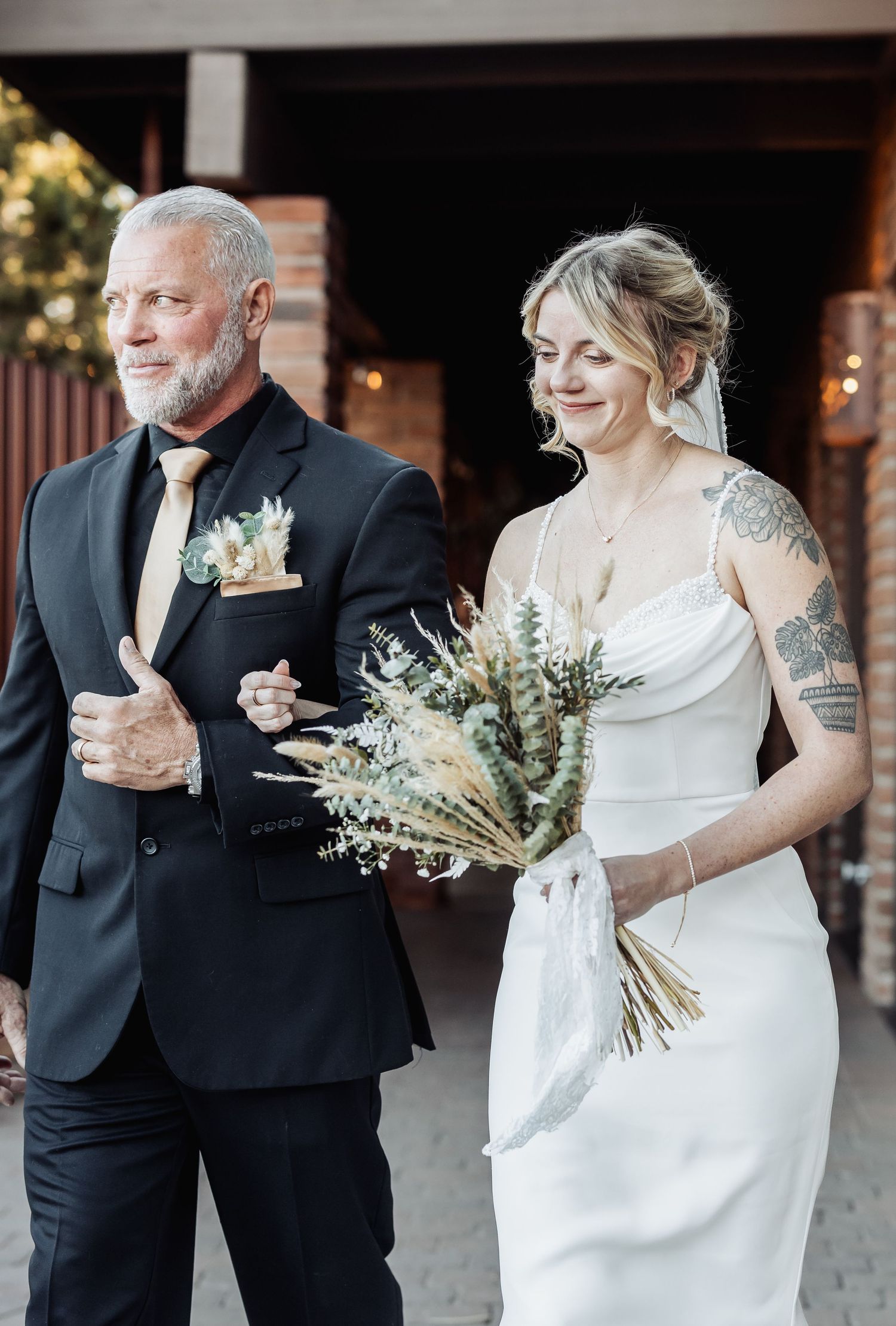 Elegant wedding couple dressed in white gown and black tuxedo holding a rustic dried flower bouquet.
