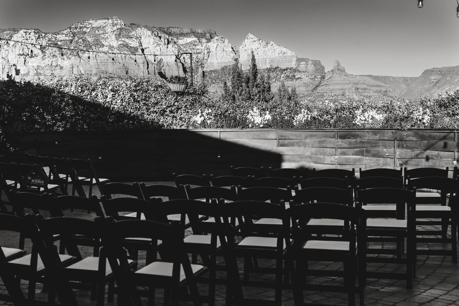 A black and white panoramic view of canyon cliffs with rows of dark chairs arranged in an outdoor setting.