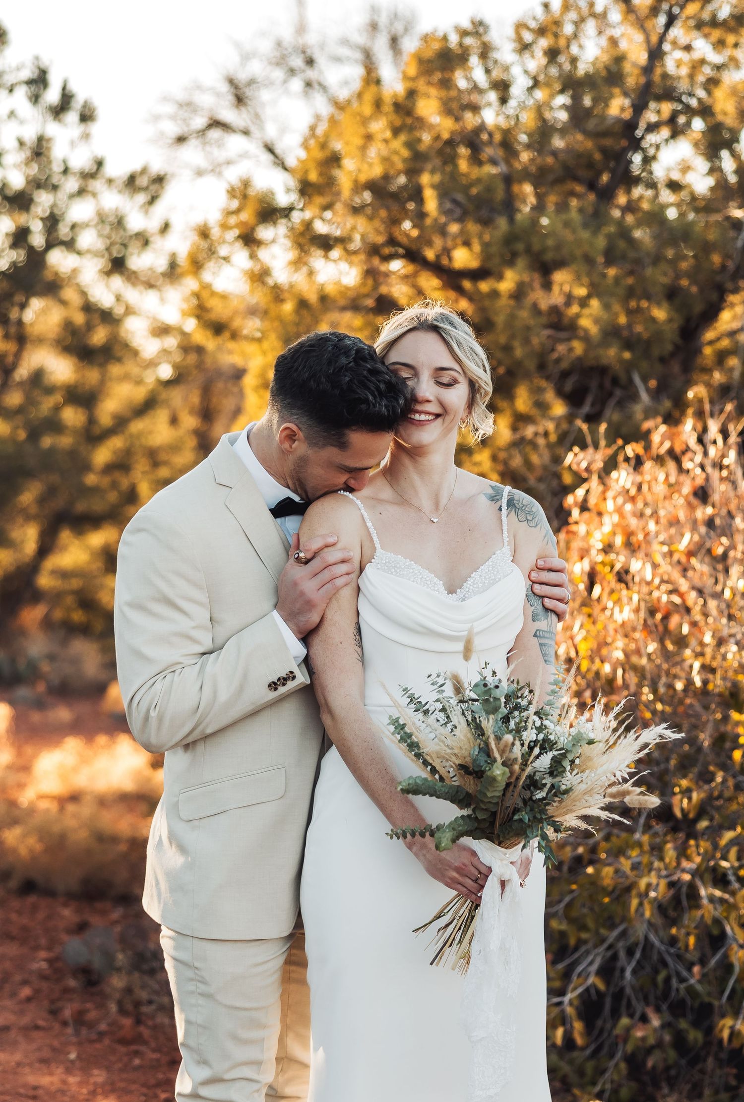 Romantic wedding moment captured in warm golden light among desert vegetation.