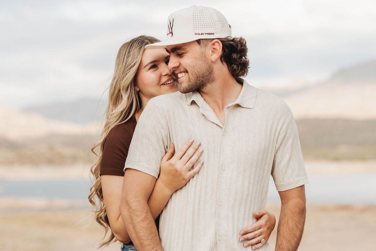 A couple shares an intimate moment together on a beach during golden hour in casual attire.
