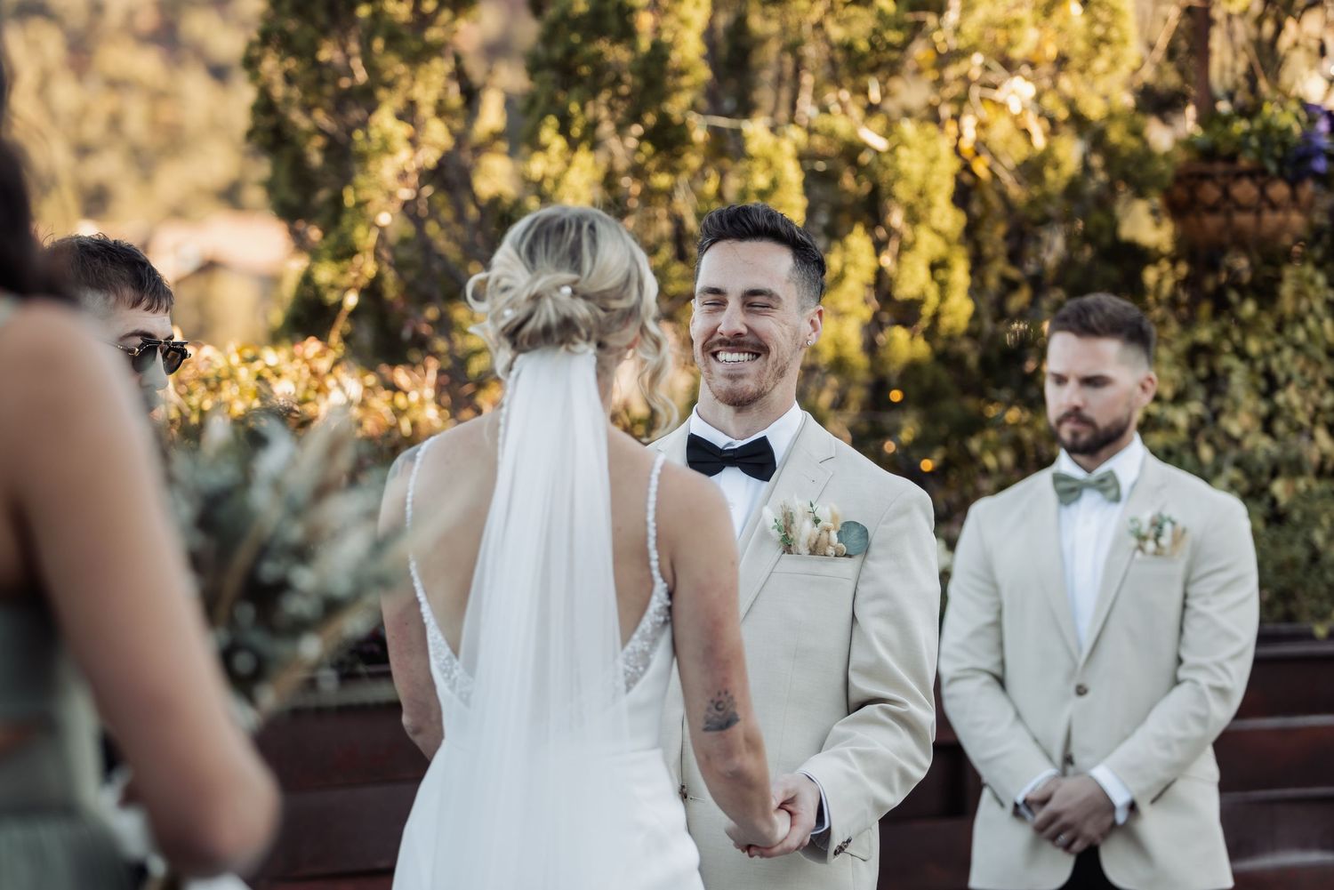 Wedding party poses outdoors in light-colored attire amidst golden autumn foliage during sunset.