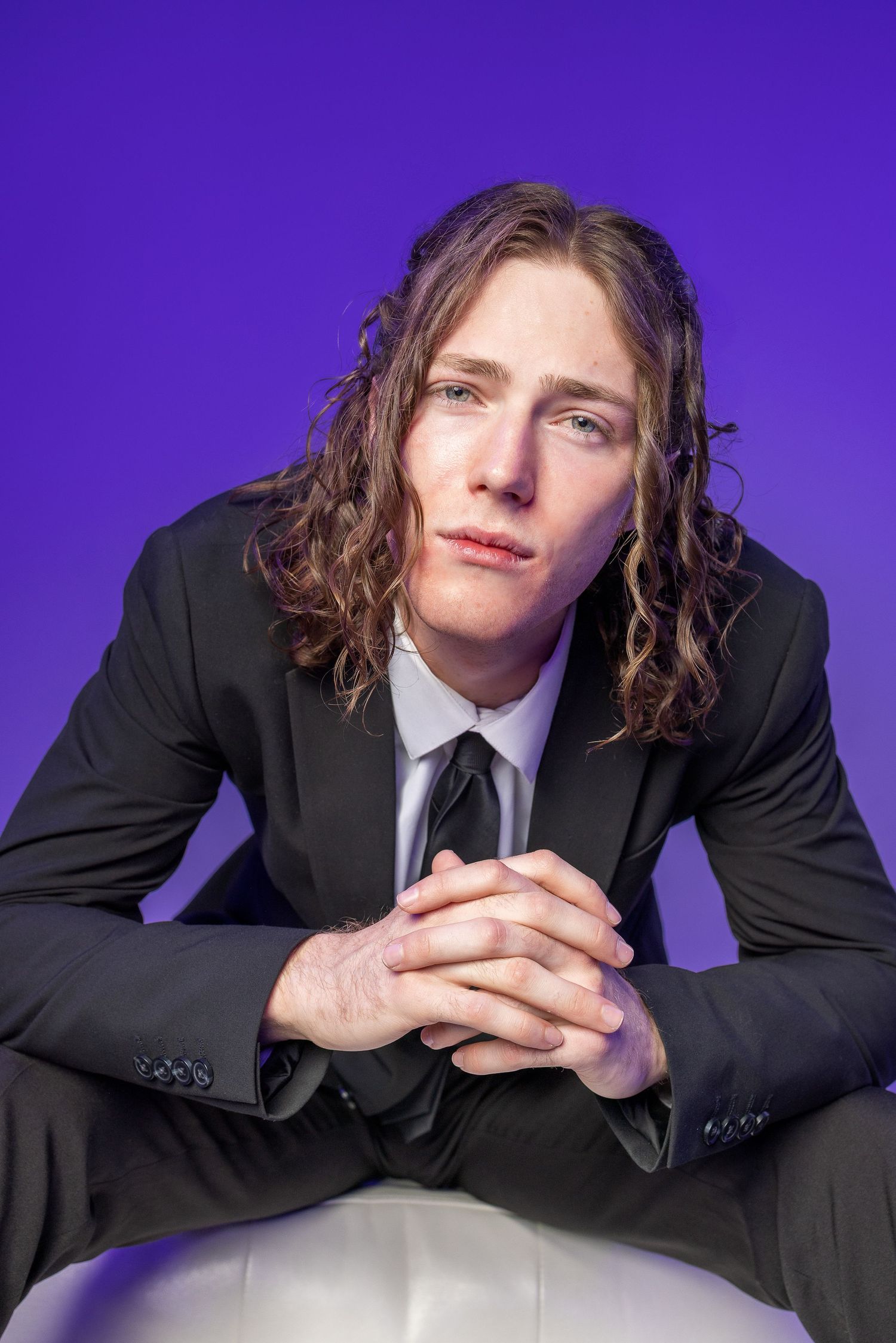 Person in black suit poses against purple backdrop showing multiple dynamic angles in casual portrait series.