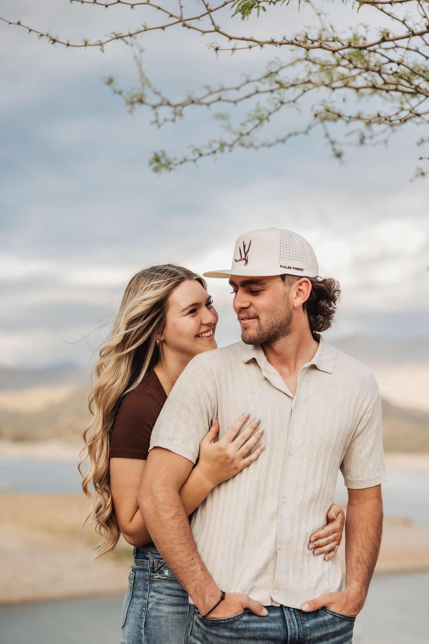 Couple enjoys romantic moment outdoors near lake with mountains and cloudy sky in background.