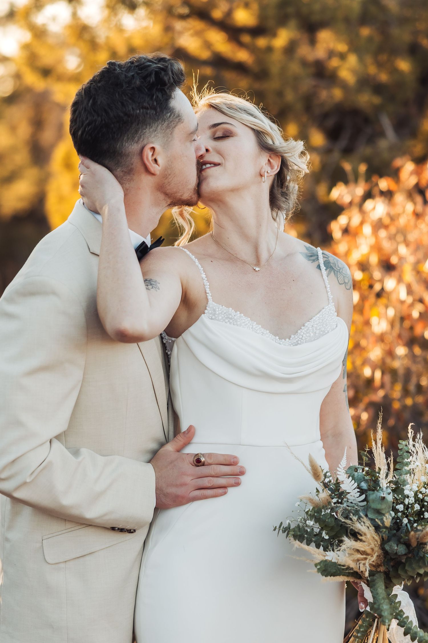 Romantic wedding moment captured in golden light with bride in flowing white dress holding dried flower bouquet.