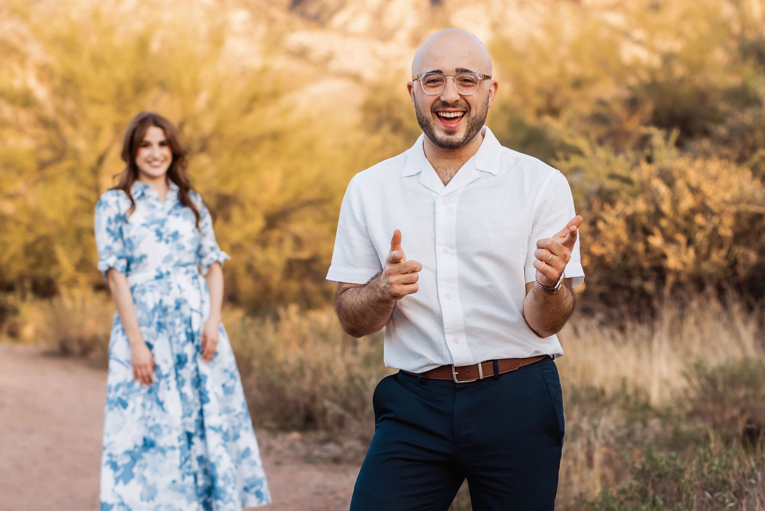 A couple in a desert setting, with someone in a white shirt gesturing excitedly and someone in a floral blue dress.