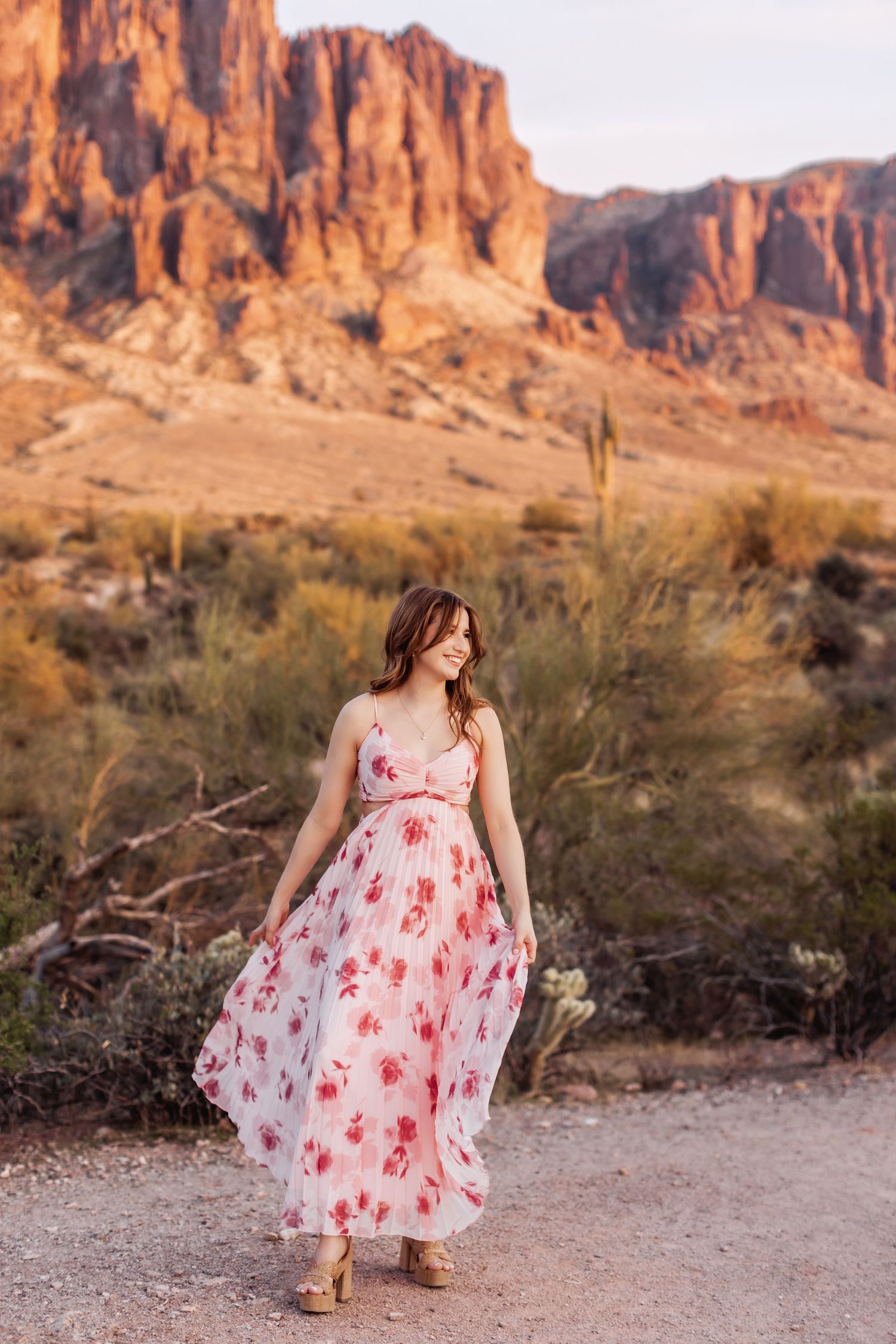A flowing pink floral dress catches the breeze against dramatic red rock cliffs in the Superstition Mountains.