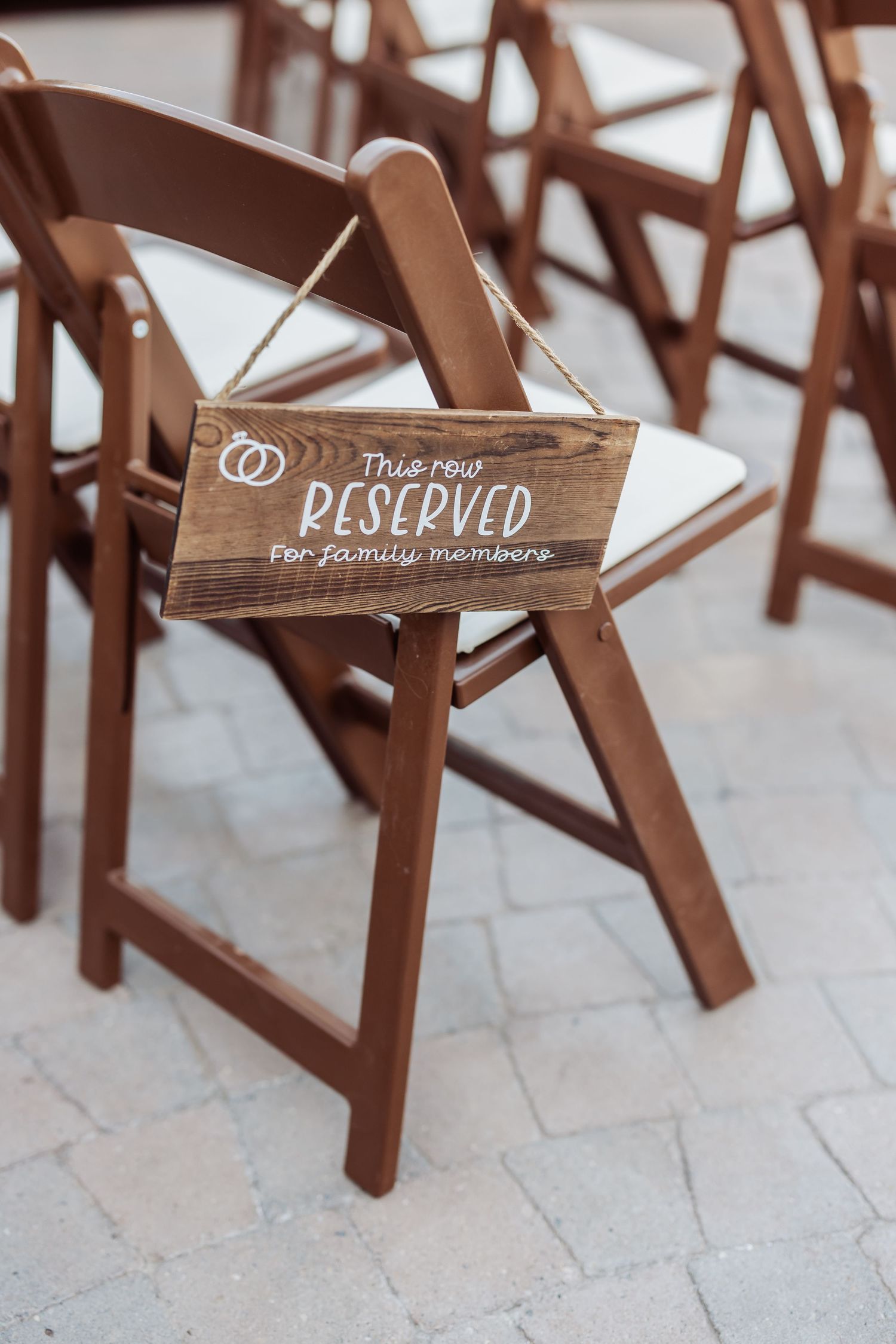 Rustic wooden reserved sign hanging on brown folding chair at wedding ceremony setup.