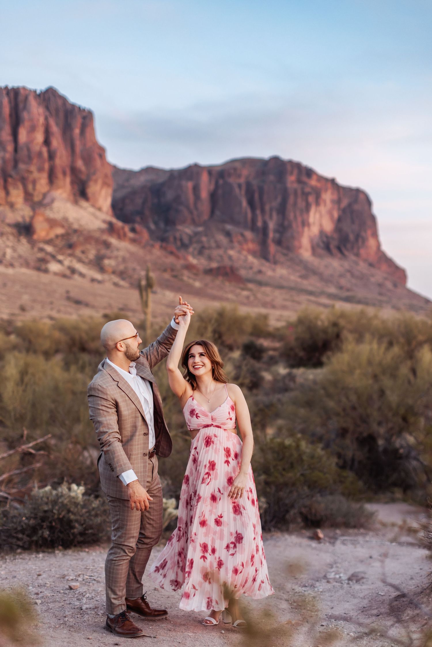 A couple dances together in formal attire against the backdrop of red desert cliffs at sunset in the Superstition Mountains.