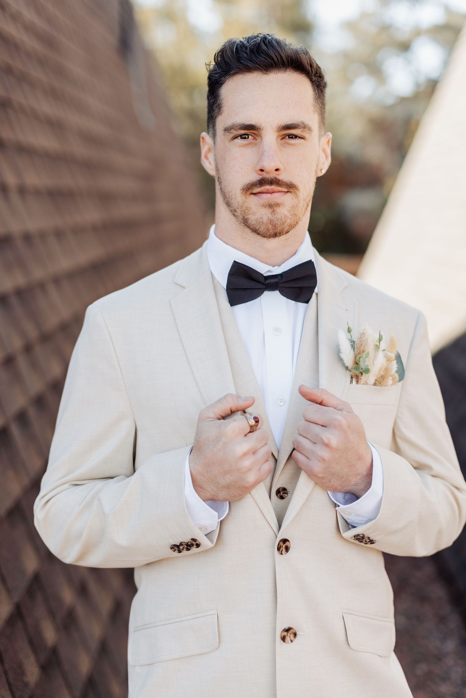 Close-up shots of someone in a cream colored suit jacket with a black bowtie against a natural background.