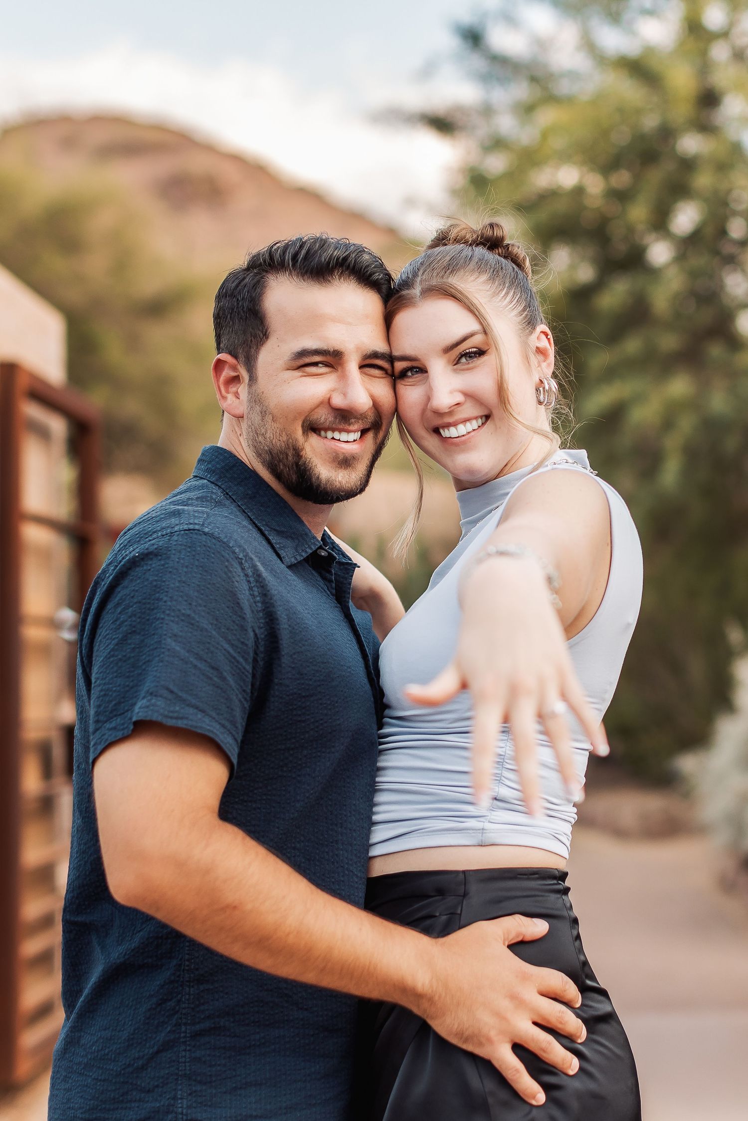 A happy couple embraces and smiles while standing outdoors in casual clothing.