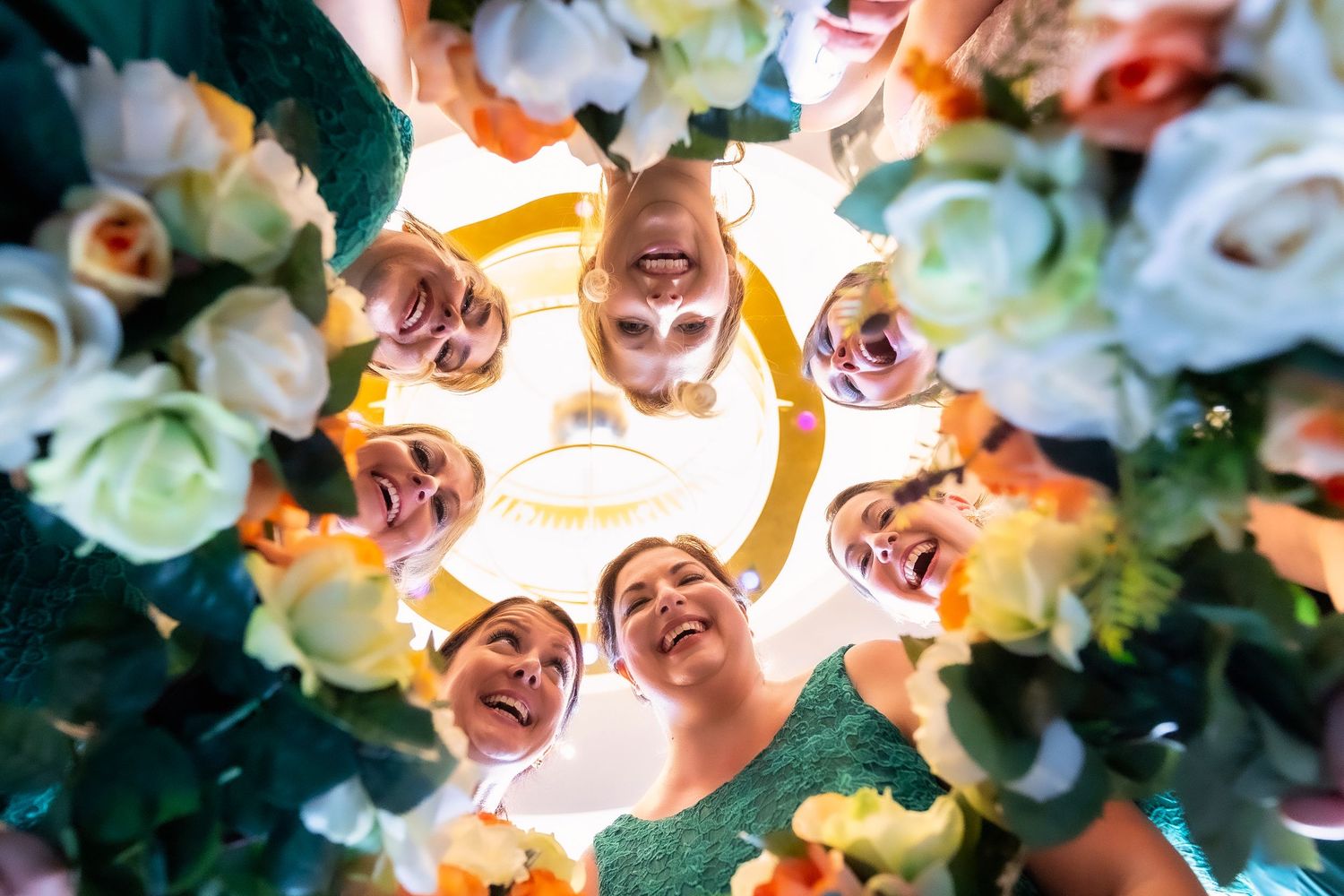 Looking up through a decorative flower arrangement of white and pink roses forming a circular frame with joyful faces above.