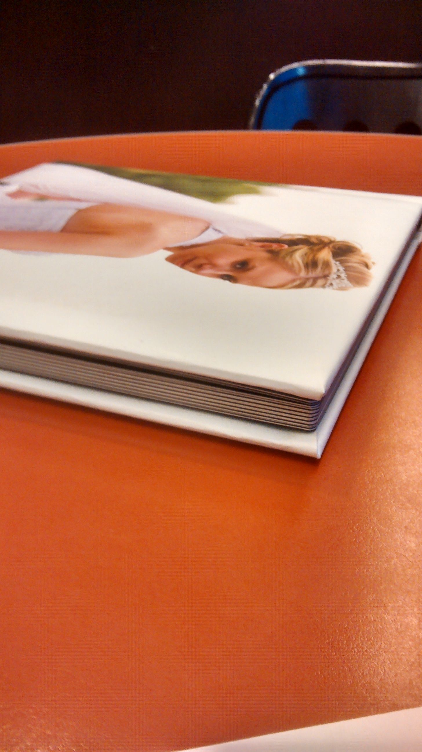 A series of image frames showing a hardcover book progressively opening on an orange surface, revealing inner pages.