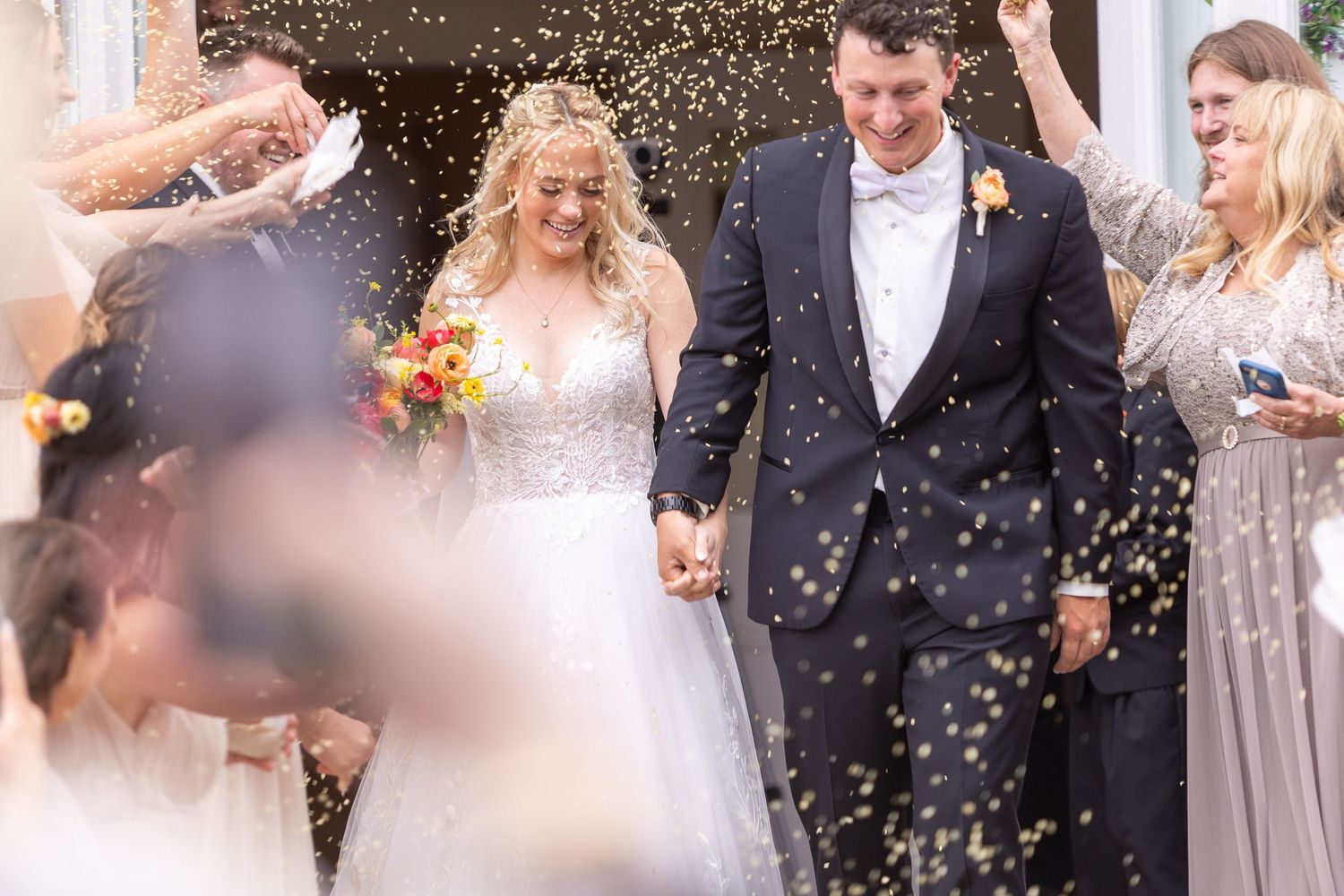 Wedding party is showered with confetti as they celebrate outdoors in elegant formal attire.
