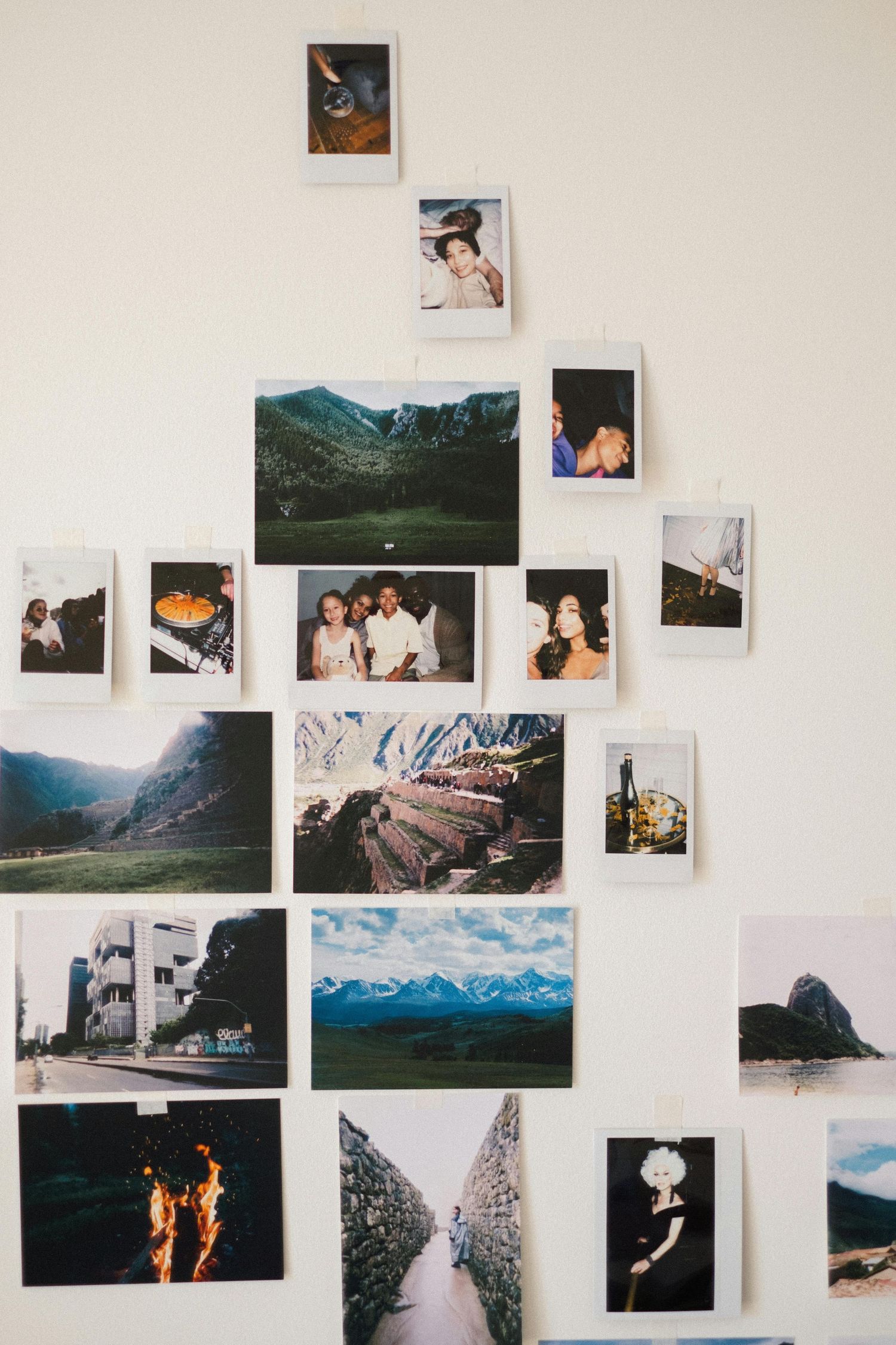 A collection of polaroid photos arranged on a white wall featuring landscape shots, mountains, and candid moments.