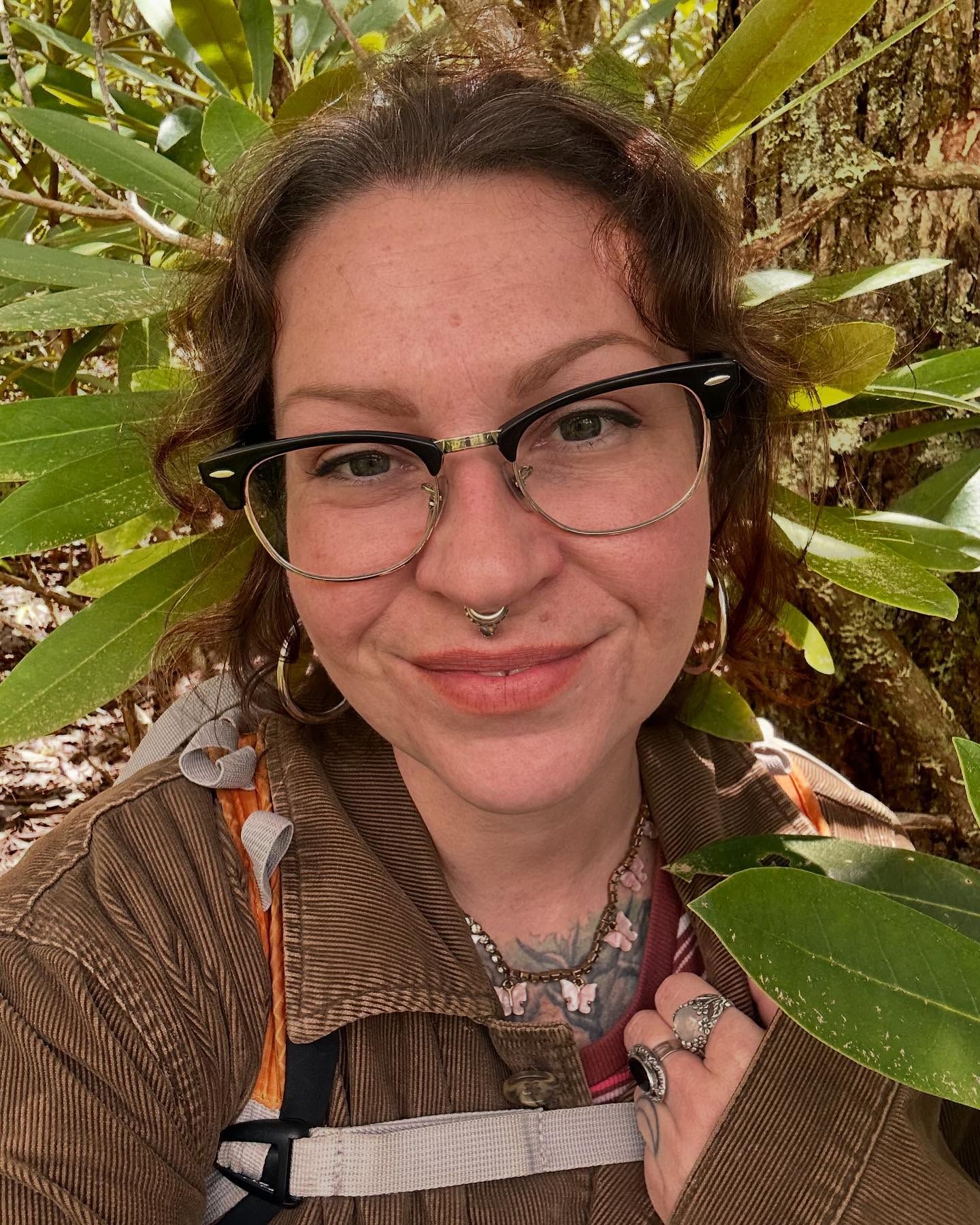 Close-up portrait of Anne Kirk against foliage showing glasses and a warm smile.