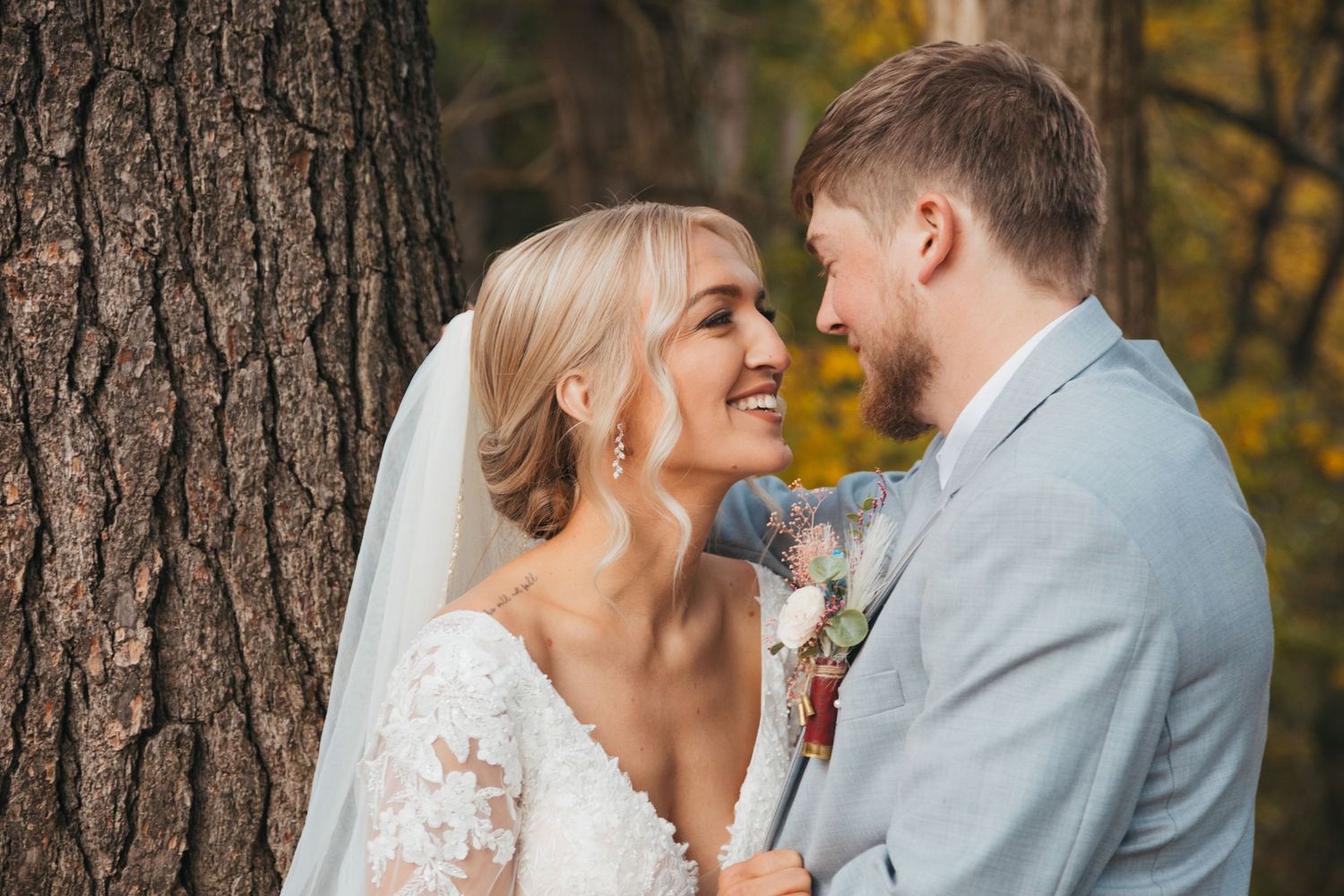 A romantic autumn wedding portrait of a couple against a large tree trunk.