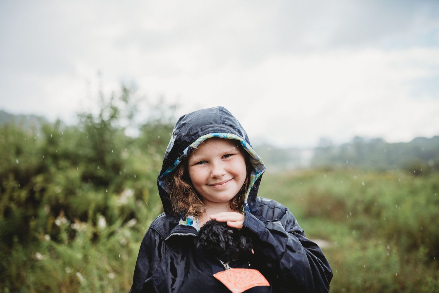 A rainy day portrait in a natural outdoor setting wearing a navy rain jacket.
