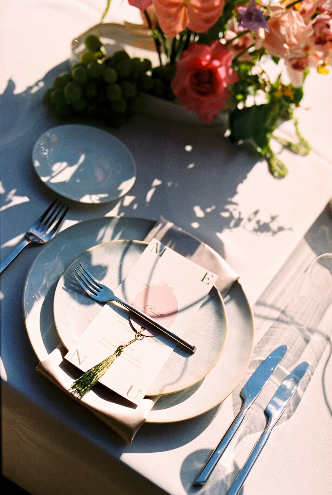 Table setting with white plates, silverware and pink flowers casting dramatic shadows in natural sunlight.