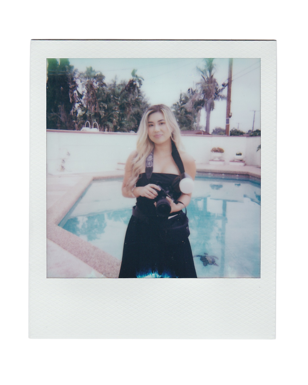 Retro polaroid-style photo showing a person in a black dress standing by a swimming pool on a sunny day.