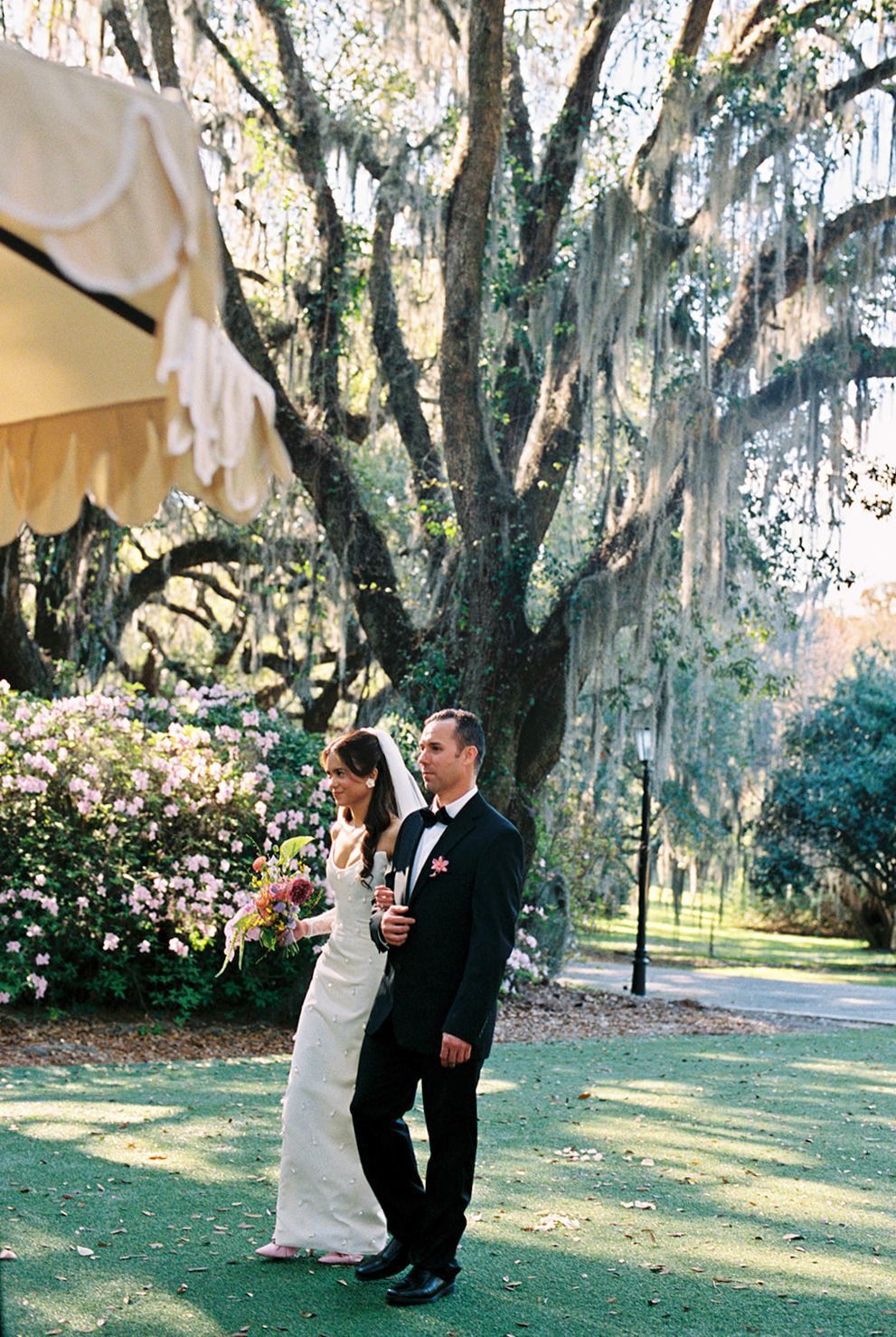A couple shares a romantic moment under Spanish moss-draped trees in a Southern garden wedding setting.