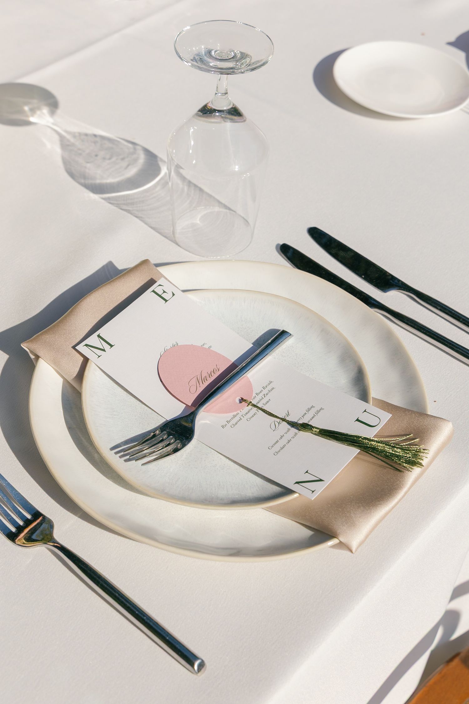 A formal table setting with white plates, silverware, and a pink menu card with rosemary sprig on crisp white linens.