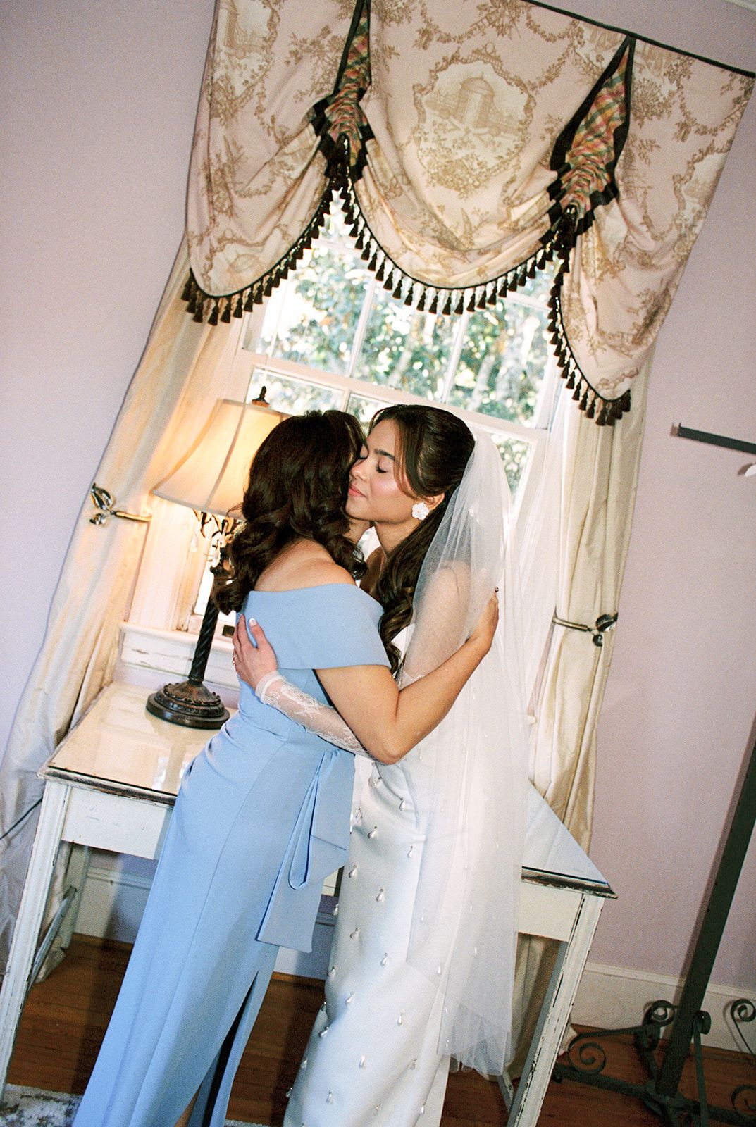 A person in a light blue dress adjusts details on a wedding dress displayed on a mannequin in an elegant room.
