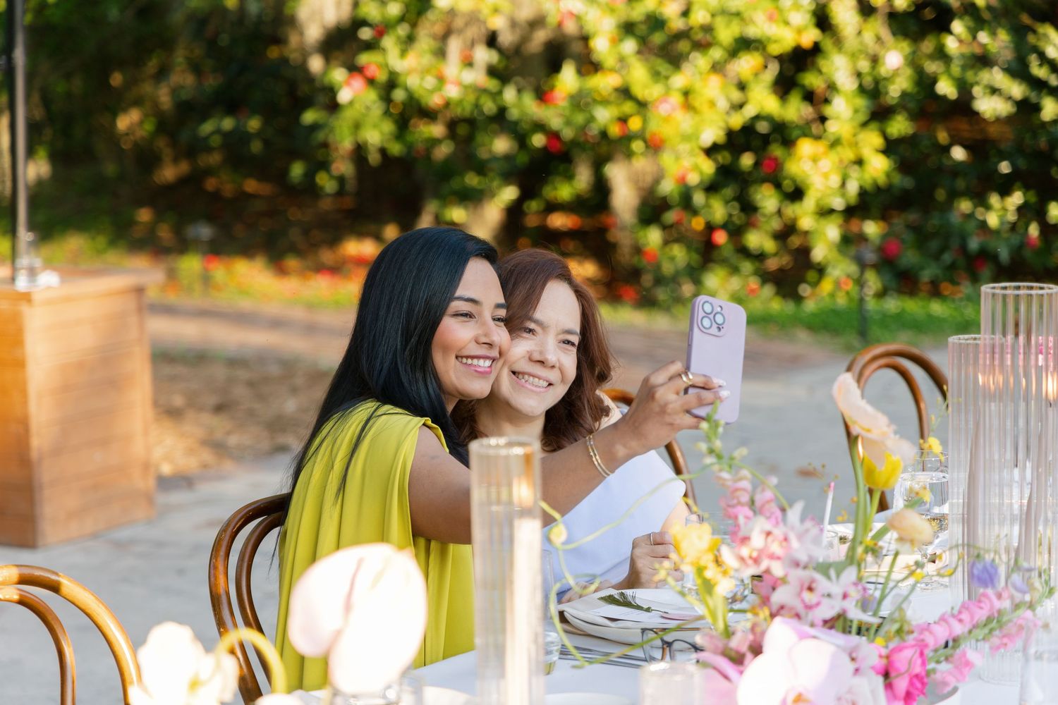 An outdoor wedding reception table decorated with pink flowers and glassware during golden hour sunlight.