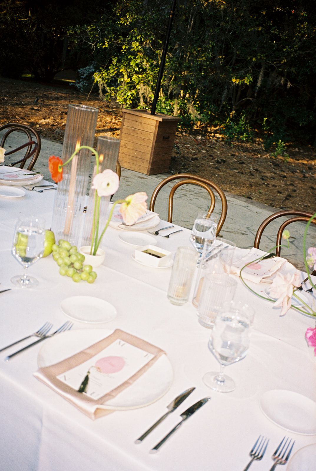 An elegant table setting at an outdoor dinner party features white plates and wine glasses against a crisp white tablecloth.