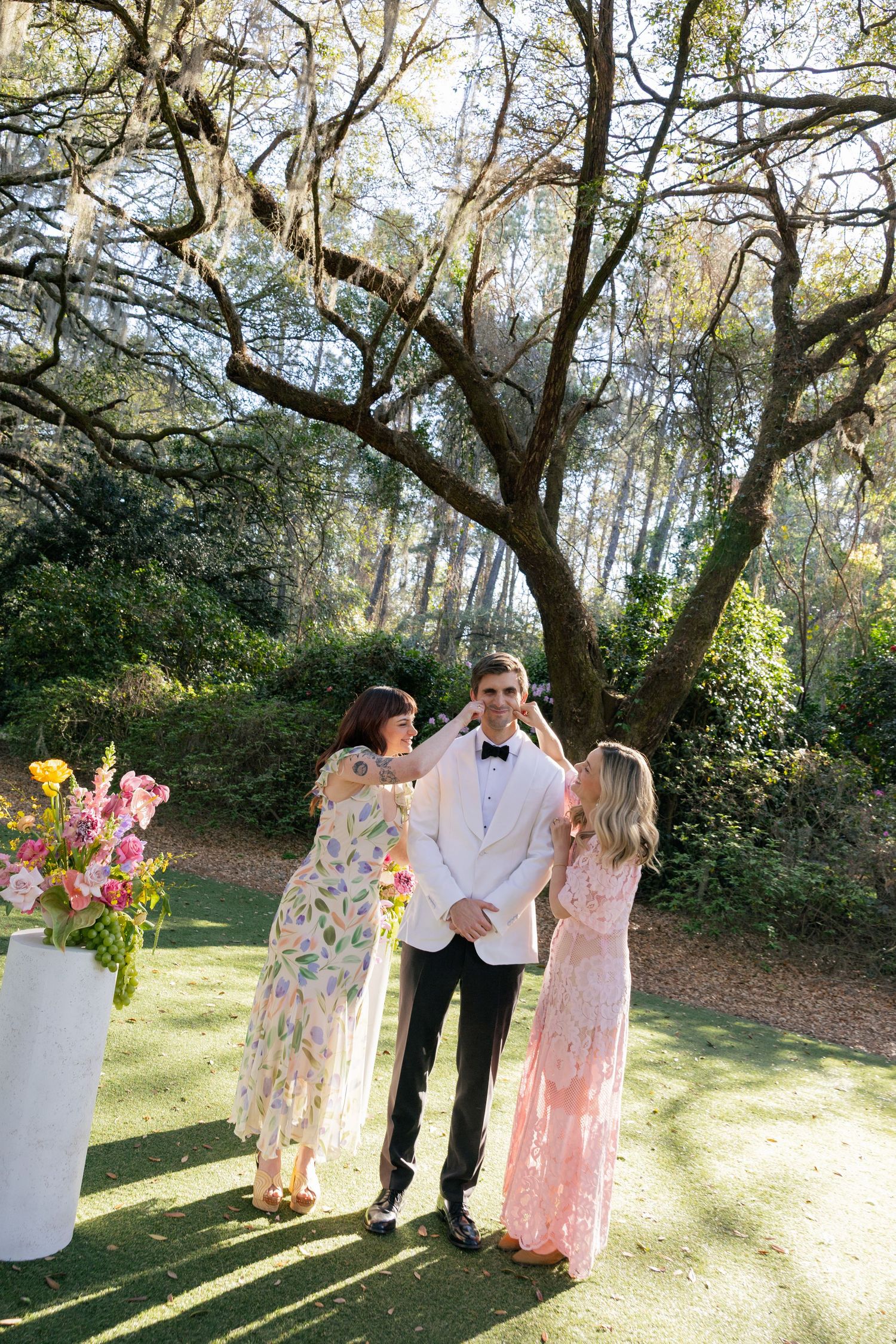 A loving couple shares an outdoor garden photoshoot with a floral backdrop and soft sunlit scenery.